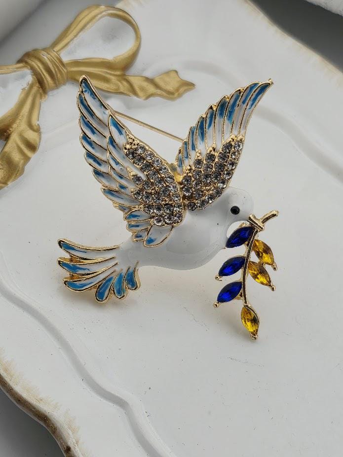 A decorative brooch in the shape of a bird, with blue and yellow gemstones on its beak and wings.