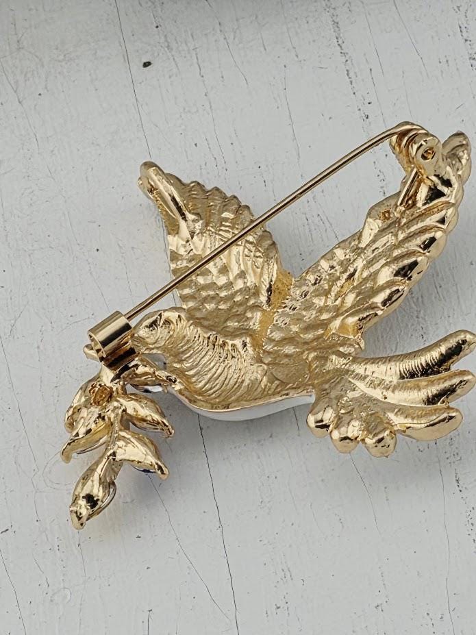 A gold-colored pin or brooch in the shape of a bird, with intricate details and a metallic sheen.