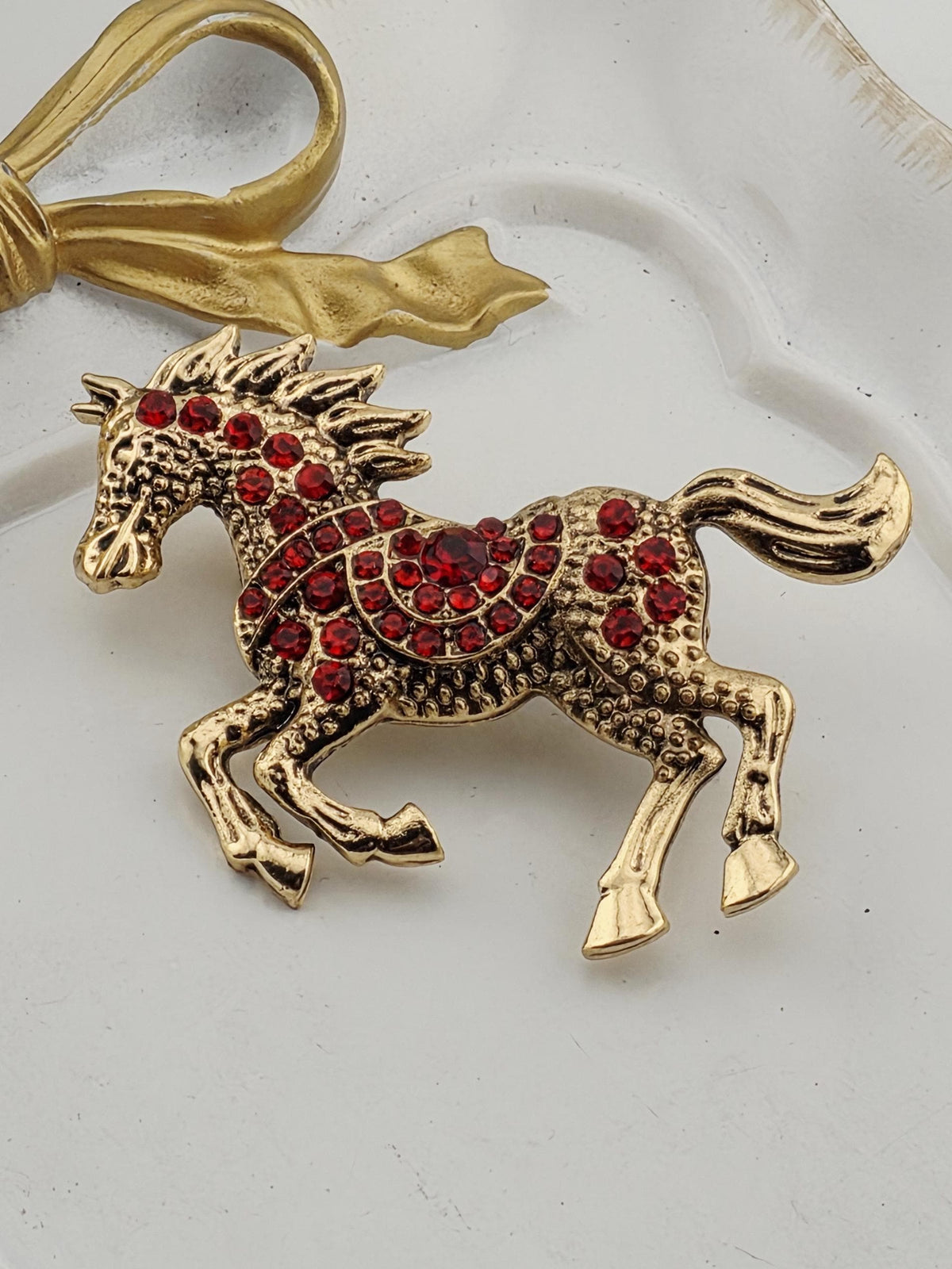 A decorative gold-colored brooch with a red gemstone in the center, resembling a horse.