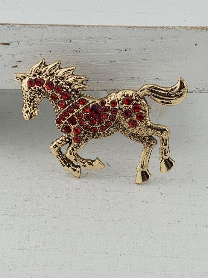 A decorative gold horse pin adorned with red gemstones.