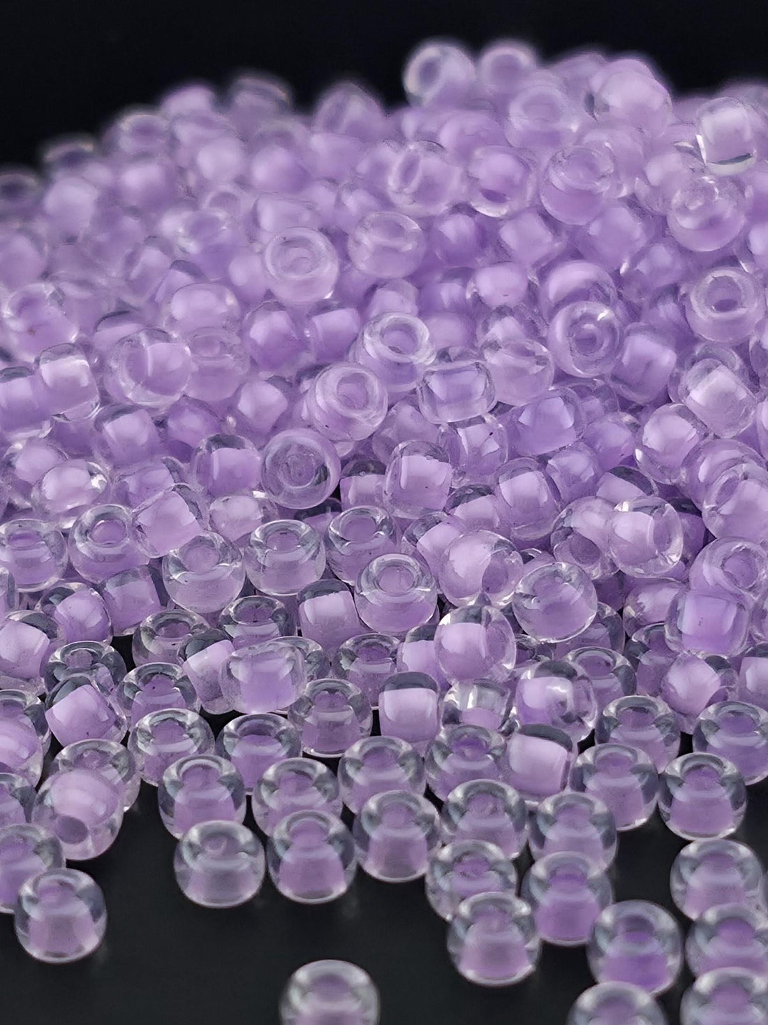 A close-up image of numerous clear, transparent beads in shades of purple, scattered across a dark background.