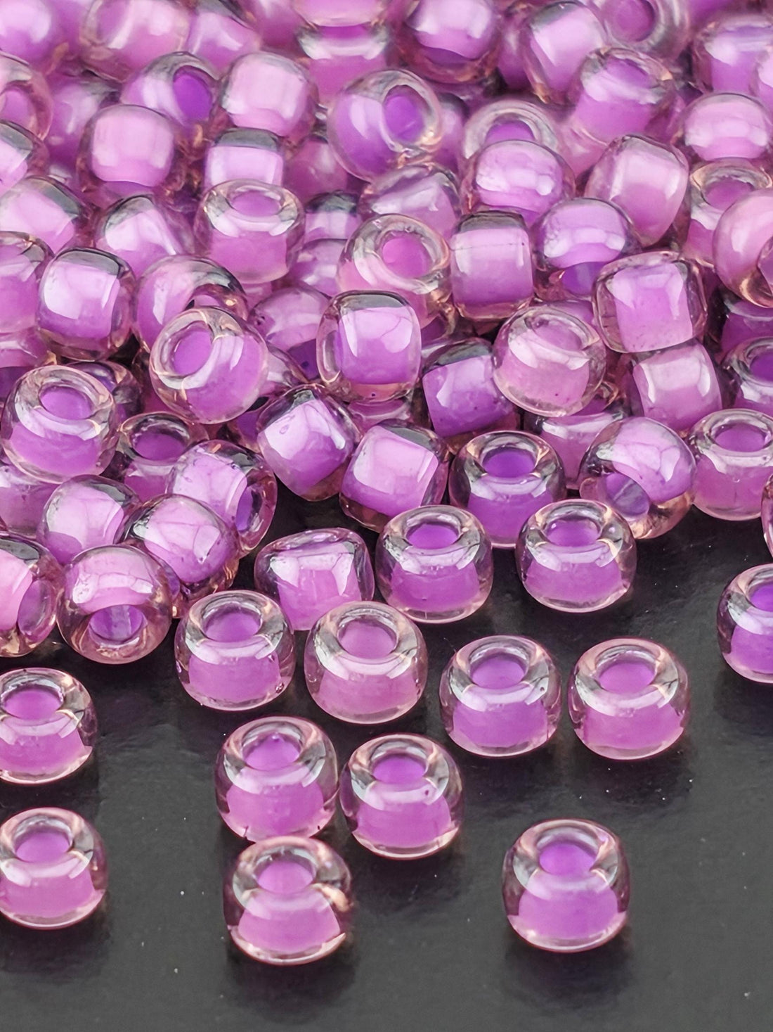 a close-up view of numerous small, clear beads in shades of purple. The beads are scattered across a surface, creating a visually striking and colorful display.