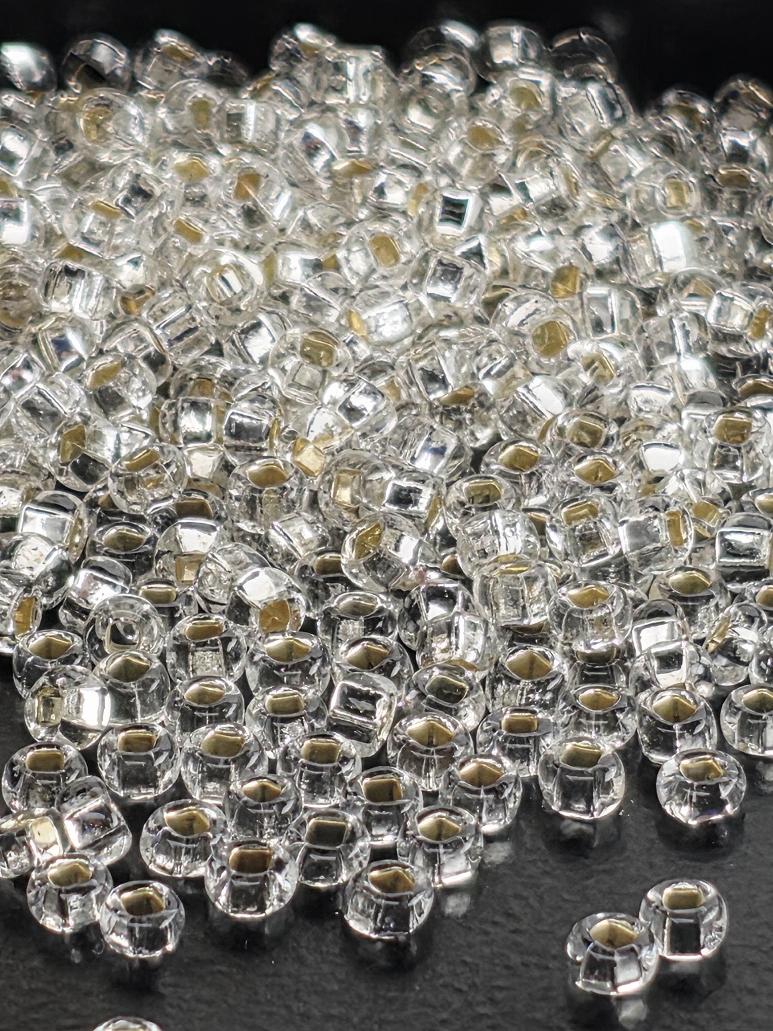A close-up image of numerous clear, shiny beads or crystals scattered on a dark surface.
