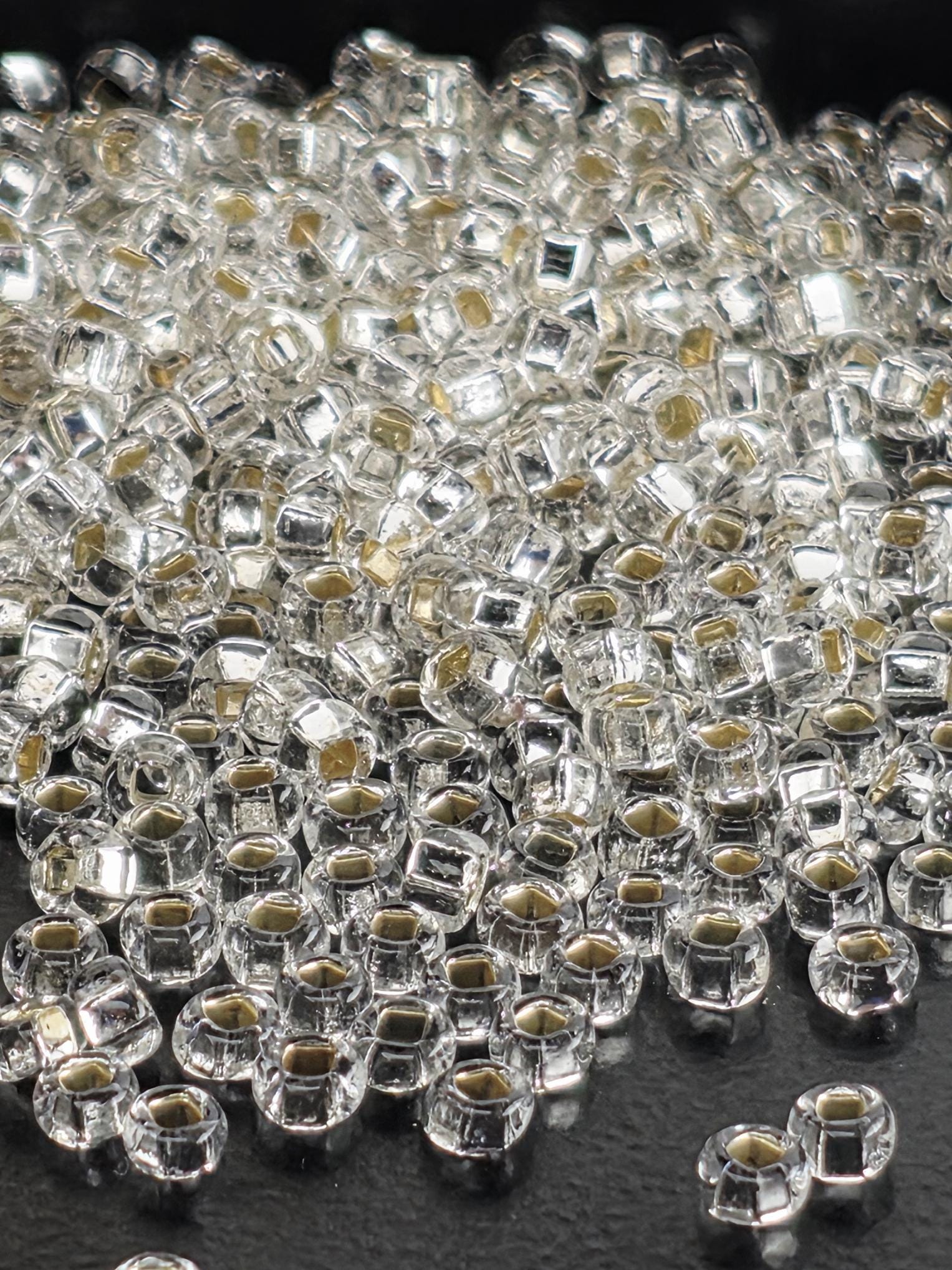 A close-up image of numerous clear, shiny beads or crystals scattered on a dark surface.