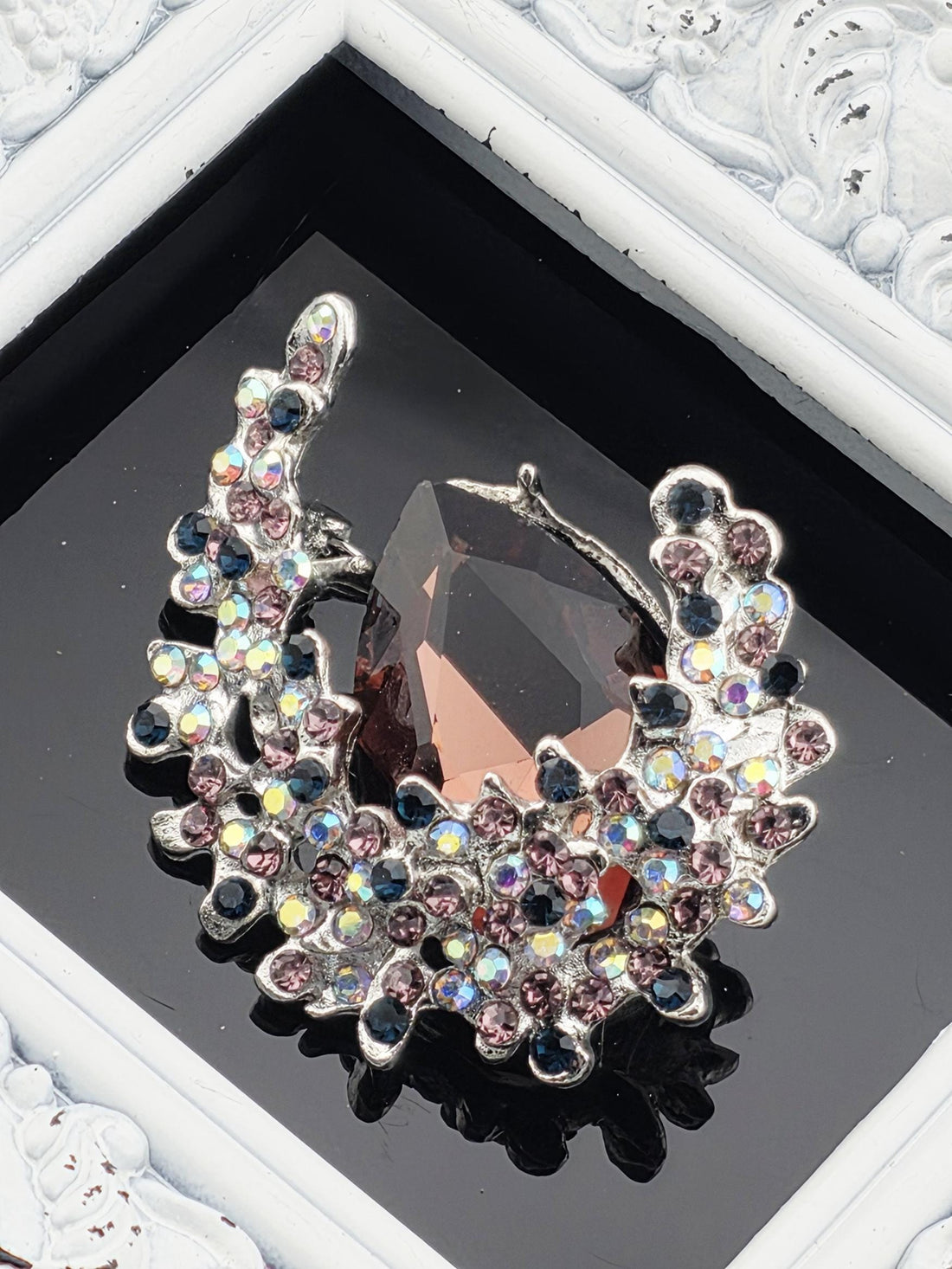 a large, ornate piece of jewelry with a dark stone and a floral design, displayed in a frame.