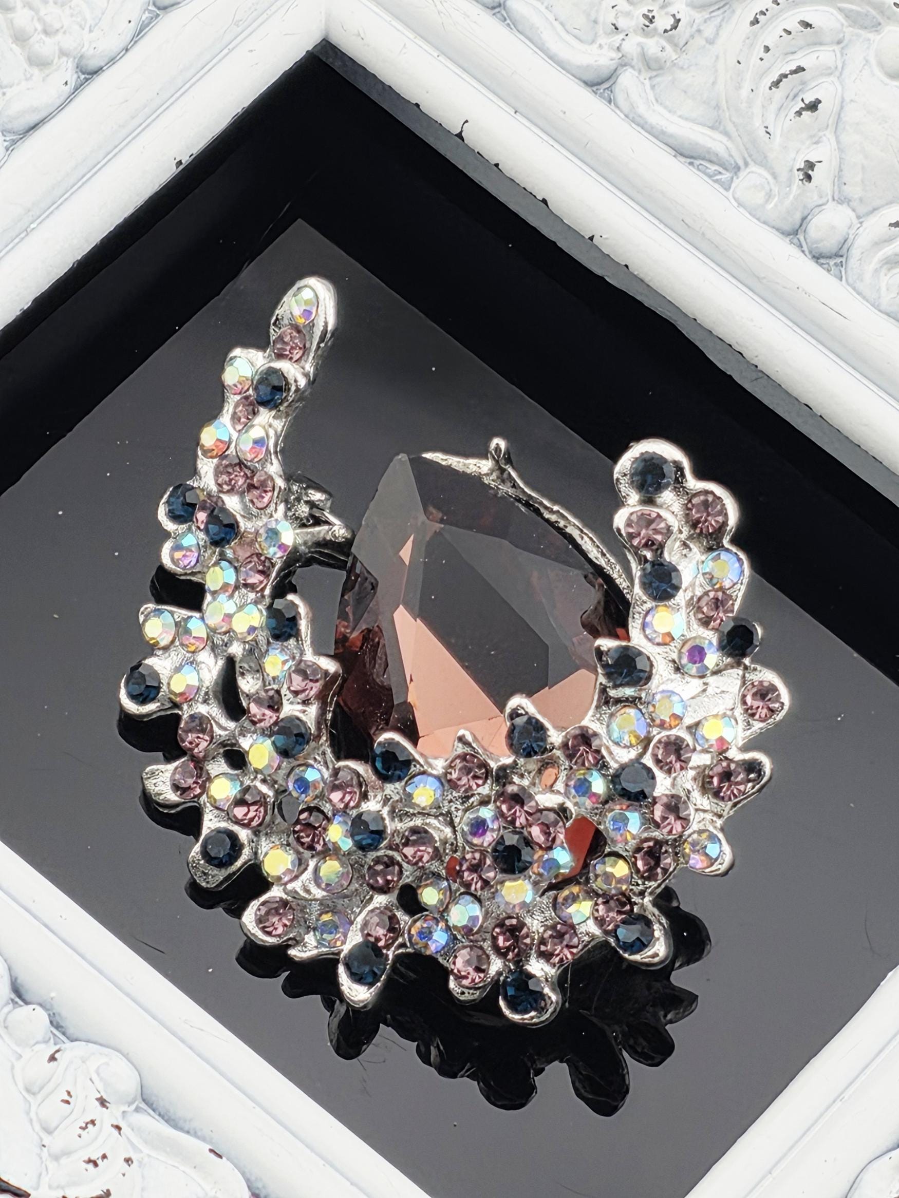 a large, ornate piece of jewelry with a dark stone and a floral design, displayed in a frame.