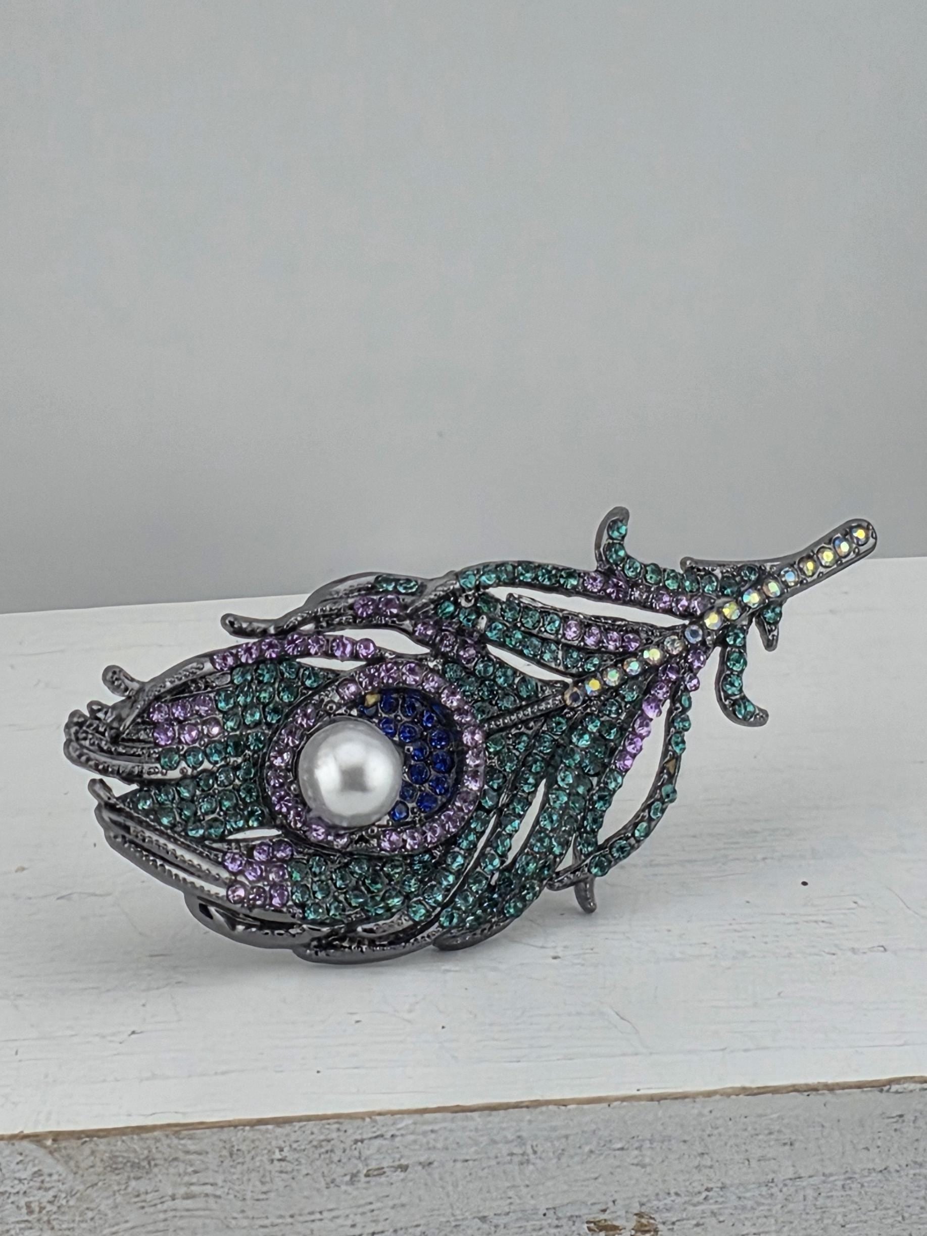 A decorative brooch with a feather-like design, featuring a central pearl surrounded by a variety of colorful gemstones.