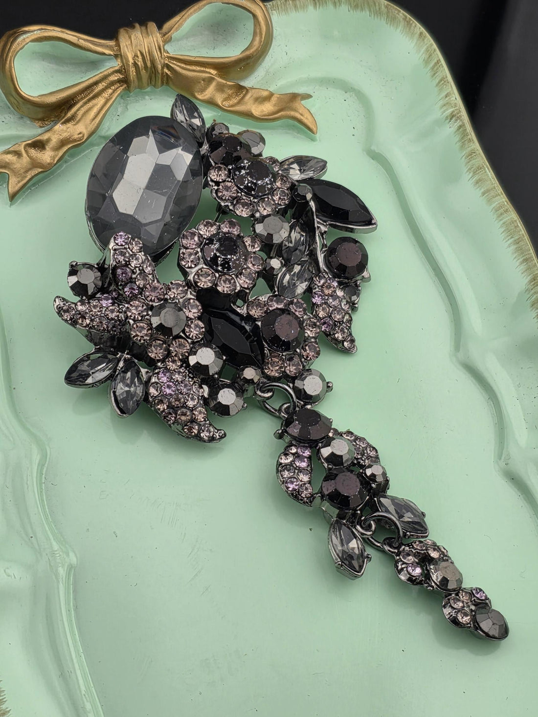 a collection of ornate jewelry, including a large crystal piece and a decorative bow, displayed on a light green tray.