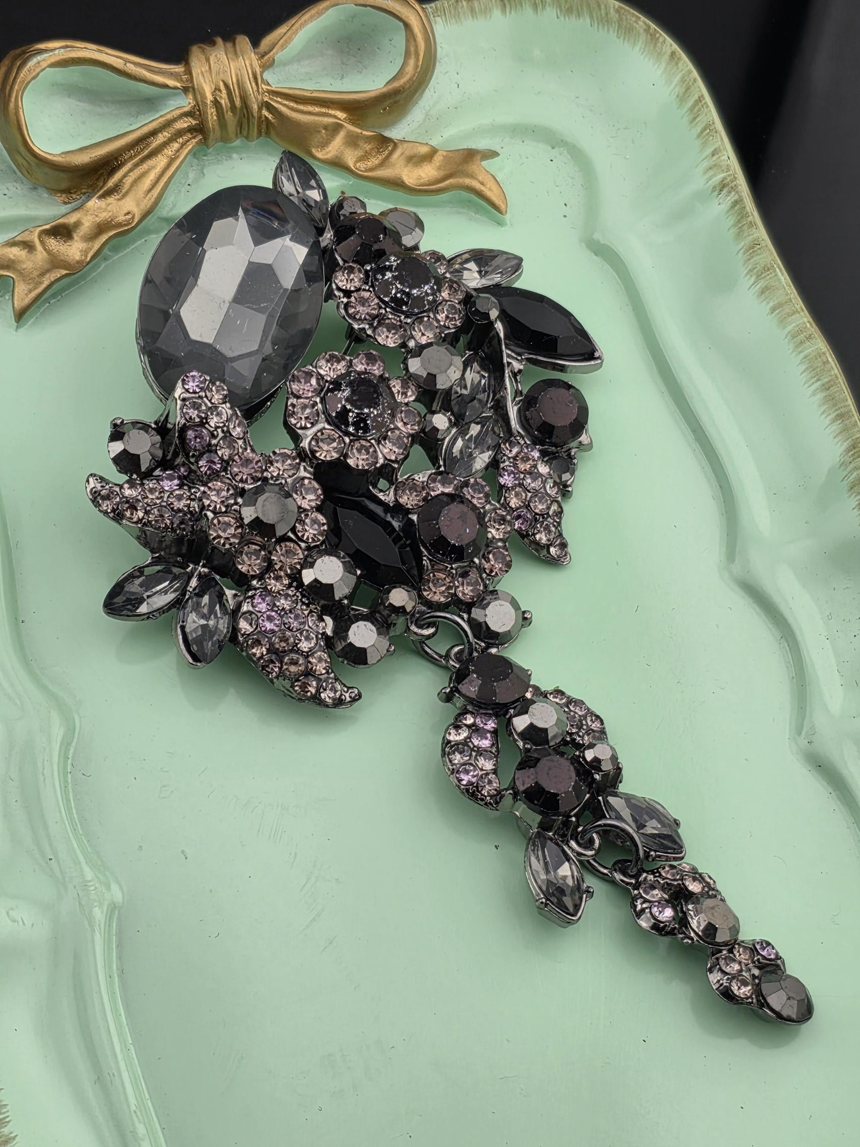 a collection of ornate jewelry, including a large crystal piece and a decorative bow, displayed on a light green tray.