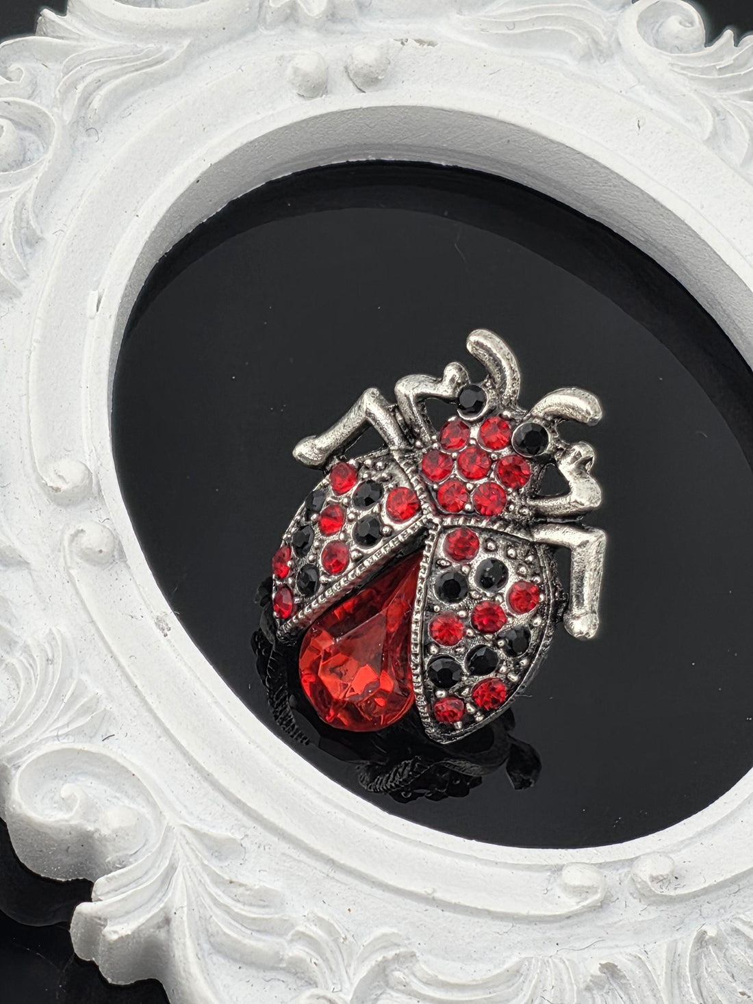 A decorative brooch in the shape of a ladybug, adorned with red and black gemstones, is displayed against a black background.