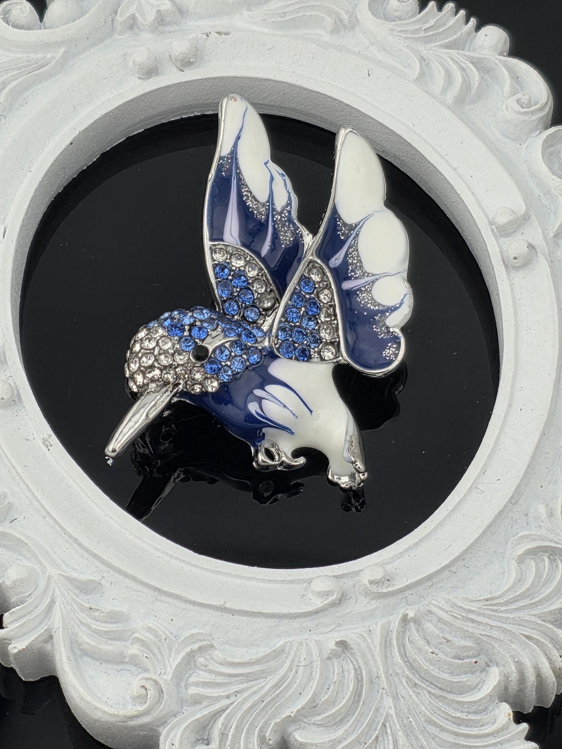 A decorative blue and white butterfly brooch with sparkling gemstones is displayed against a black background.