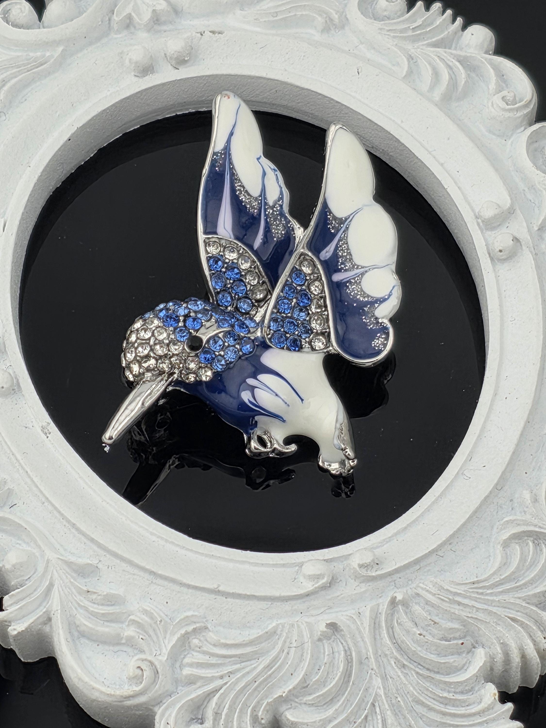 A decorative blue and white butterfly brooch with sparkling gemstones is displayed against a black background.