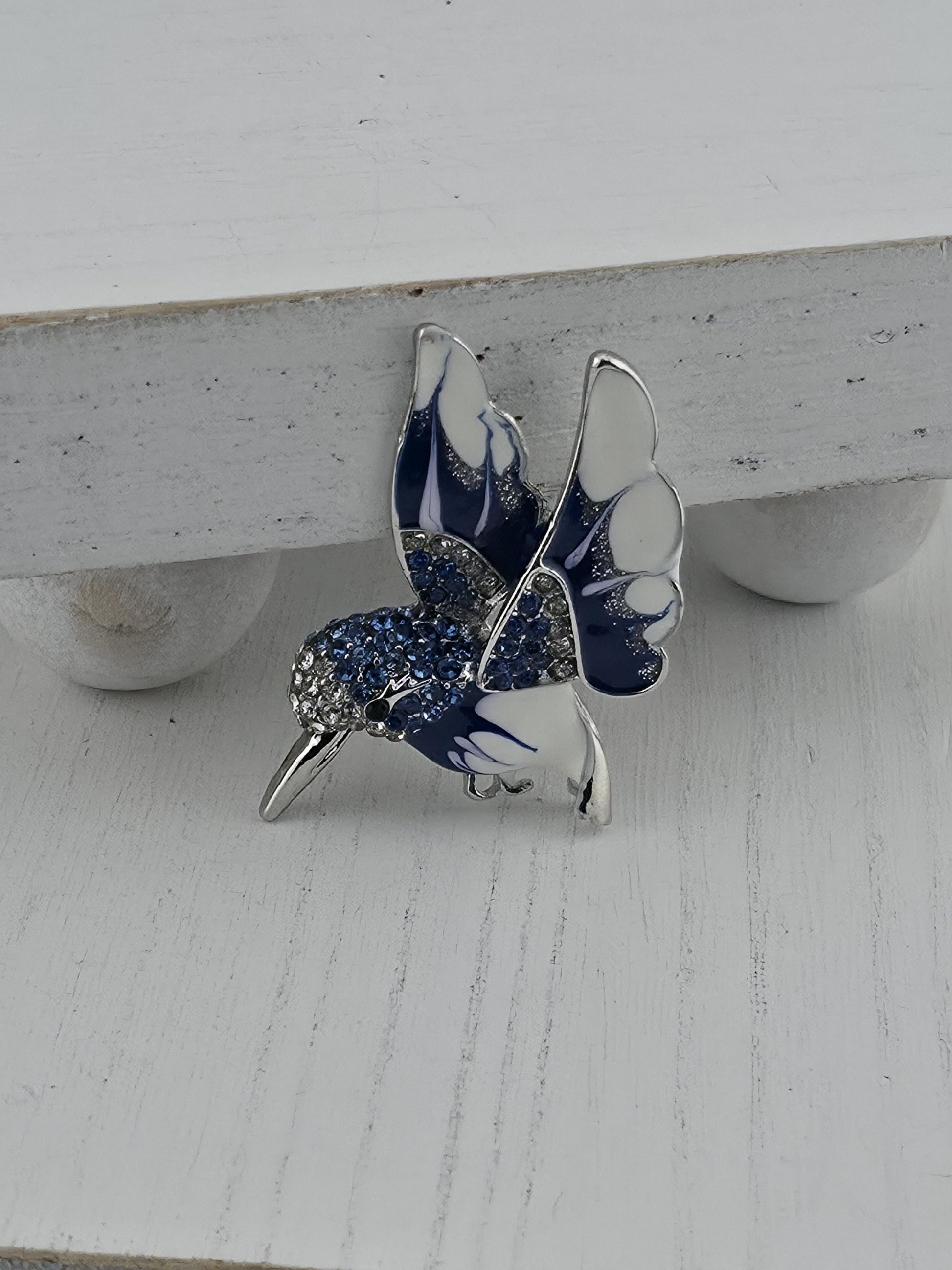A silver and blue decorative brooch with a butterfly design, featuring blue and white colors and sparkling gemstones.