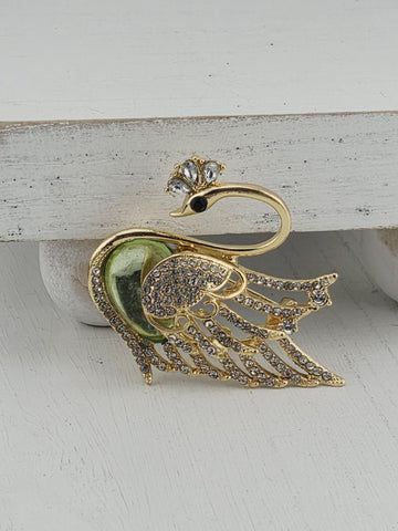 A decorative gold swan brooch with green and white accents, including a gemstone eye, is displayed against a white background.