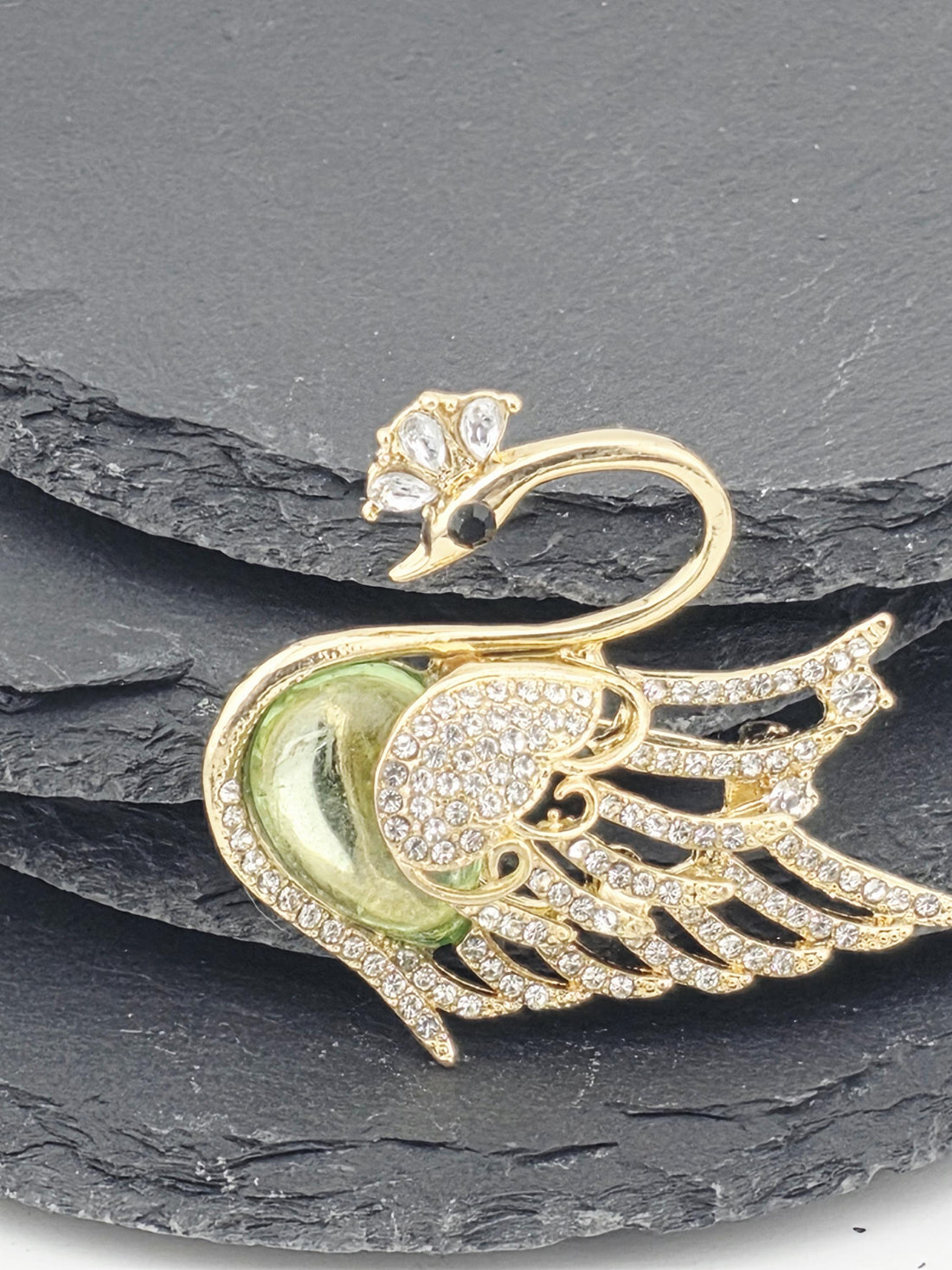 A decorative gold swan brooch with green and white accents, including a gemstone eye, is displayed against a white background.