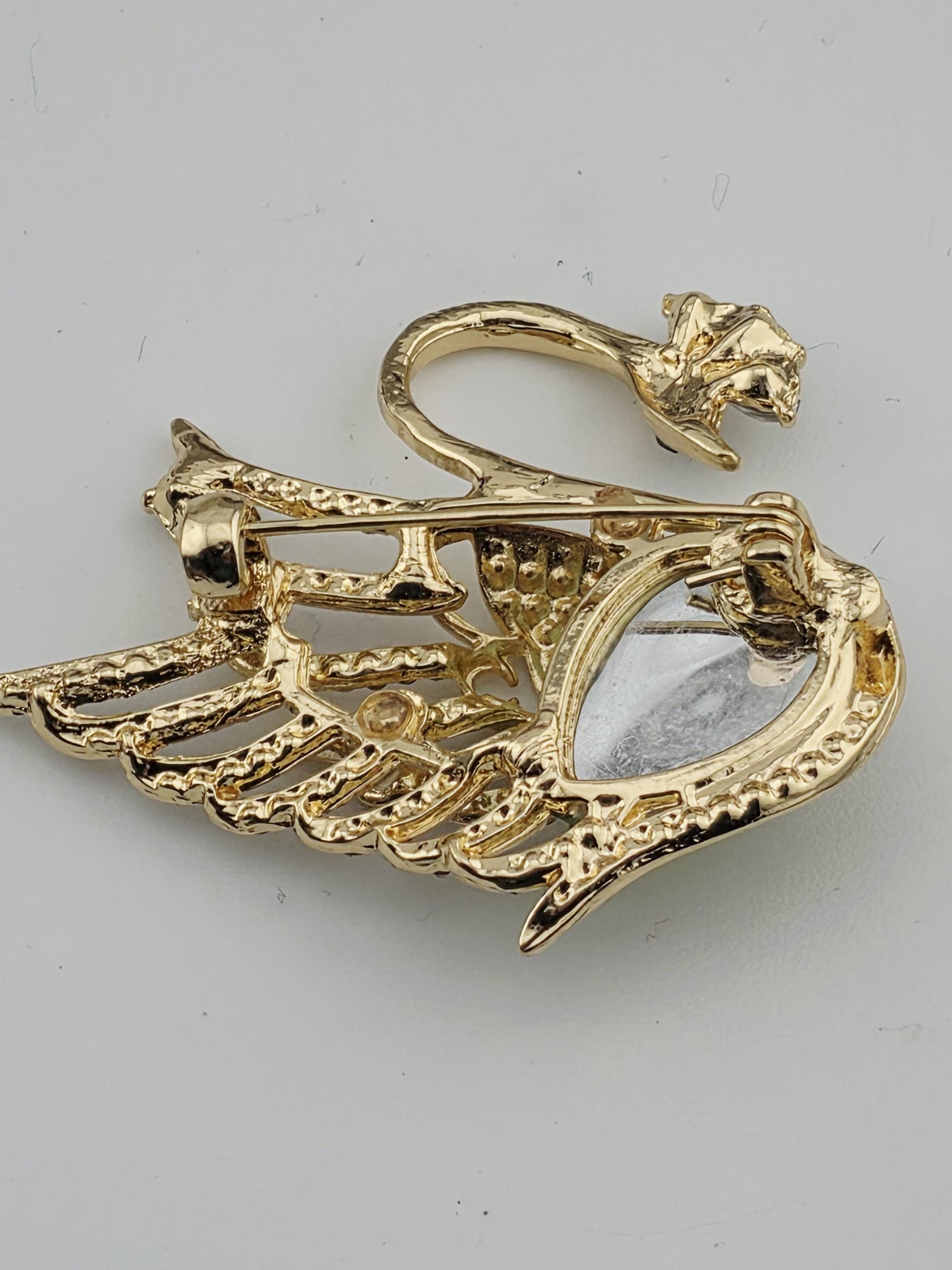 A gold-colored brooch with an intricate design, featuring a central eye-shaped element surrounded by a wing-like structure.