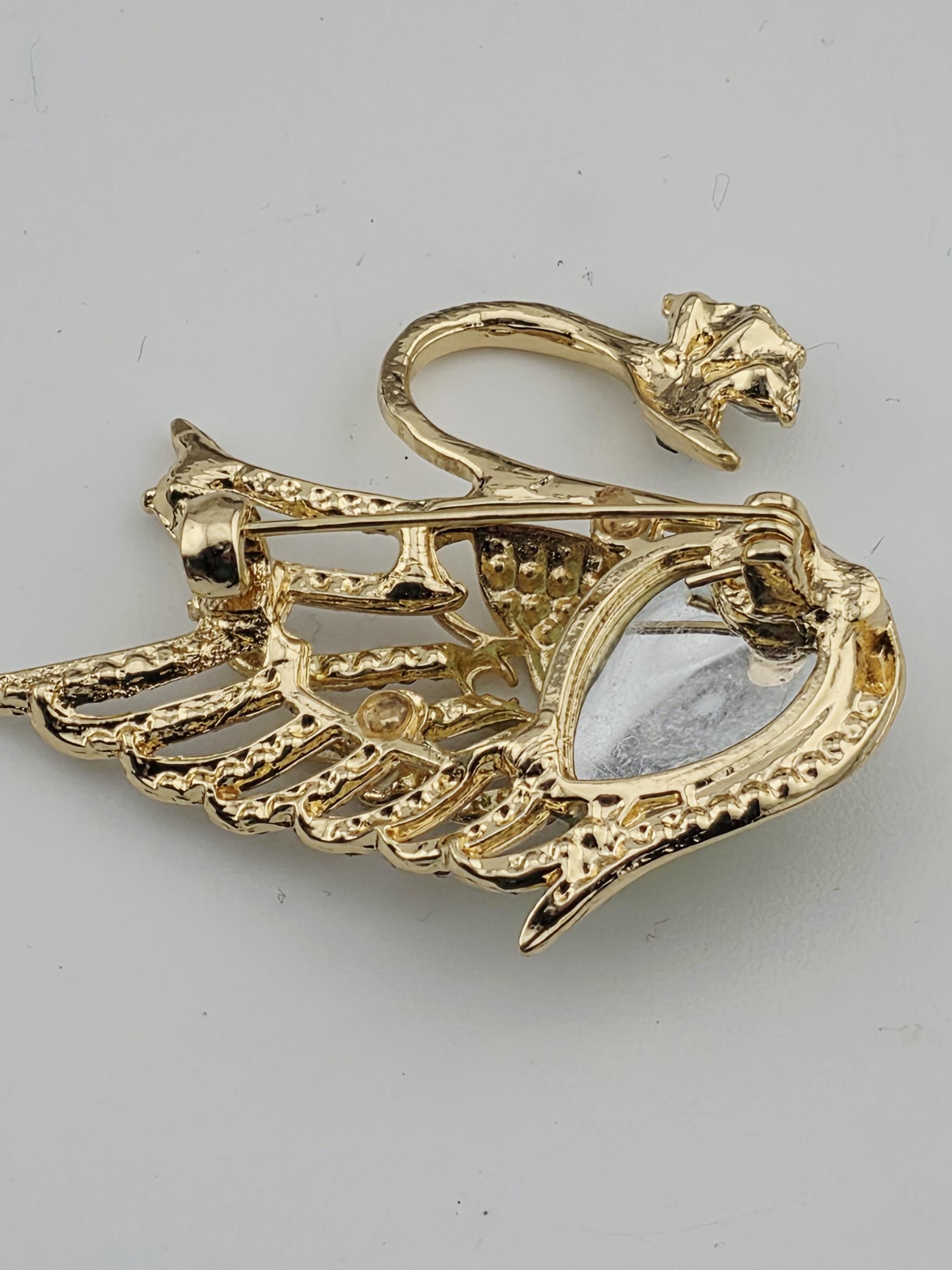 A gold-colored brooch with an intricate design, featuring a central eye-shaped element surrounded by a wing-like structure.