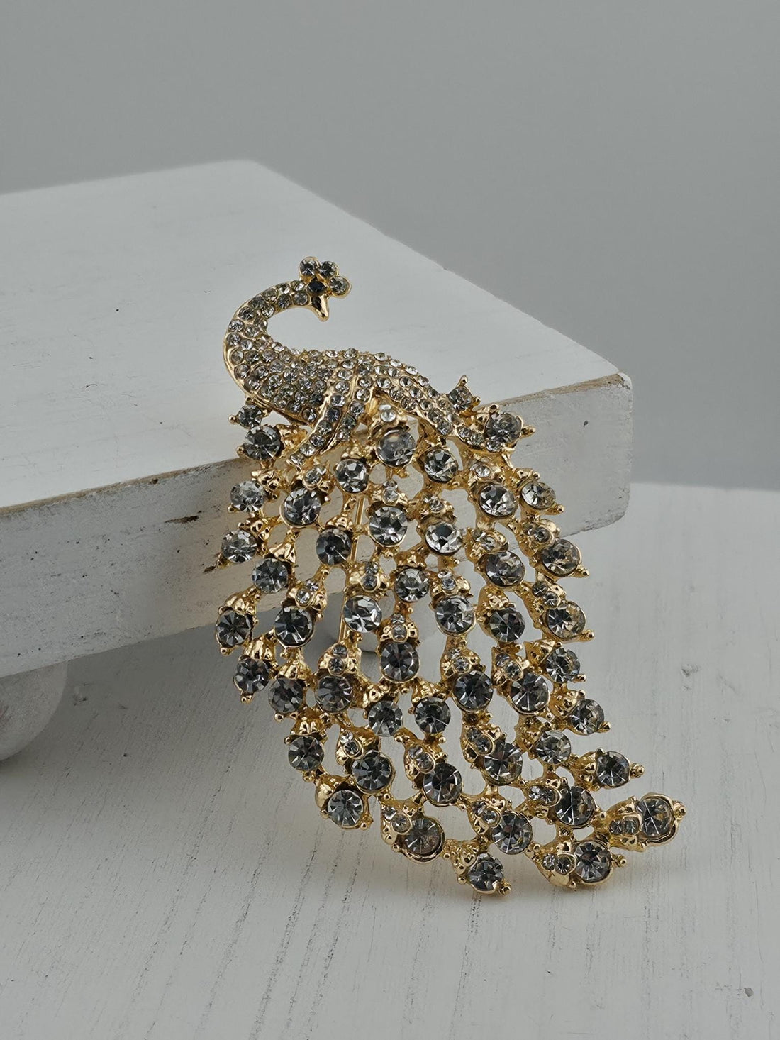 A decorative brooch in the shape of a peacock, adorned with numerous small, clear gemstones.