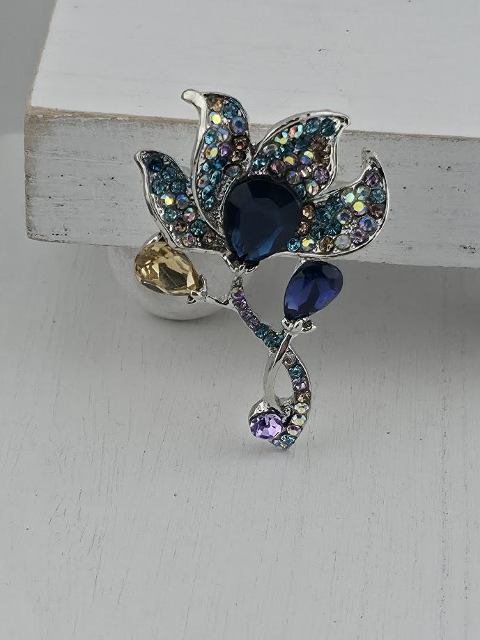 A decorative brooch with a flower-like design, featuring a combination of blue, purple, and yellow gemstones.