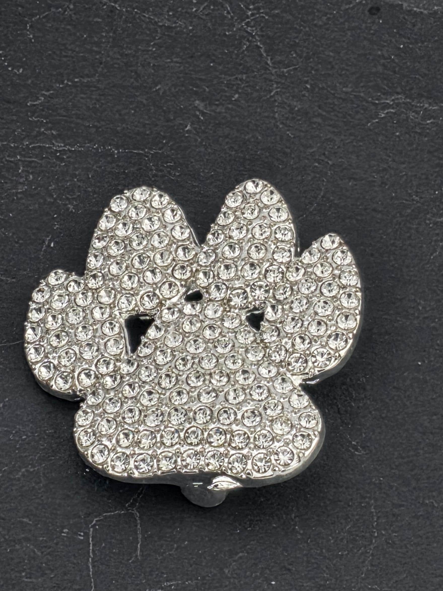 A close-up image of a silver-colored, diamond-encrusted object, possibly a piece of jewelry or a decorative item, resting on a dark surface.