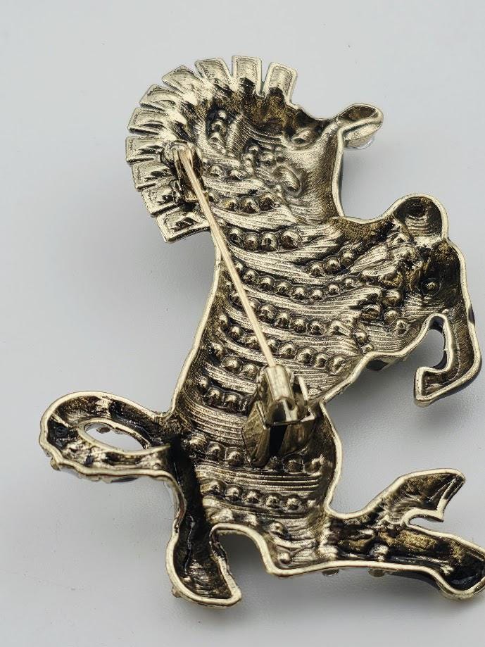 A decorative metal pin in the shape of a stylized animal, possibly a horse or zebra, with a textured and intricate design.