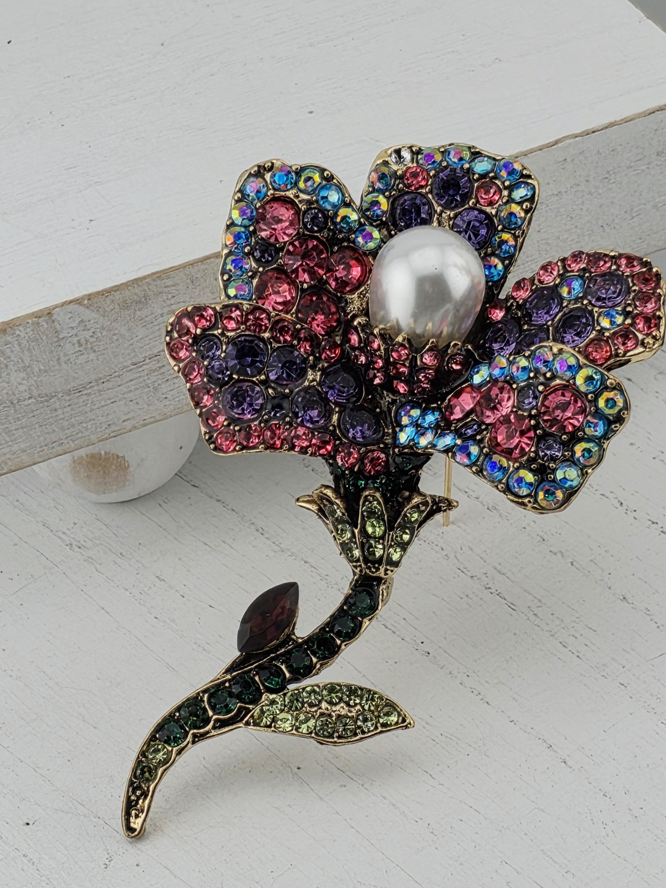 A decorative brooch with a flower-like design, featuring a variety of colorful gemstones and a large pearl at the center.
