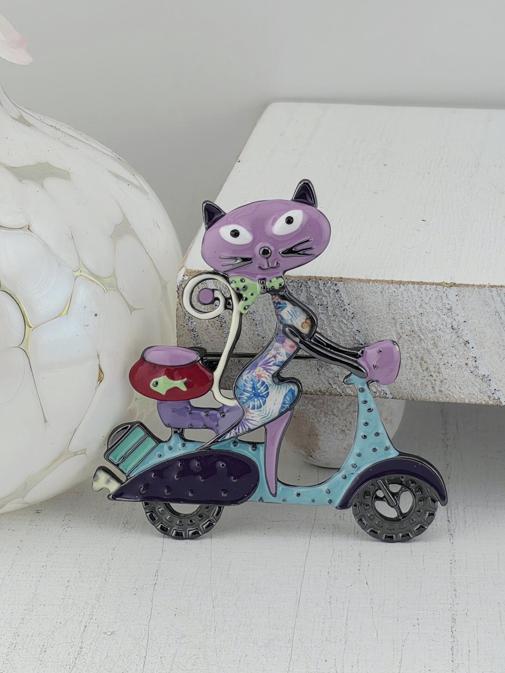 A colorful, whimsical cat-shaped object with a purple body, blue accents, and a red and green design on its head, sitting on a white surface.
