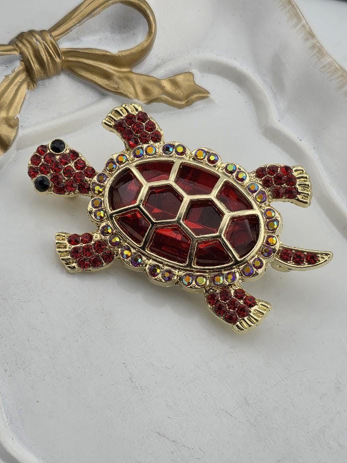 A decorative red and gold turtle brooch with a pattern of red gemstones on its shell.