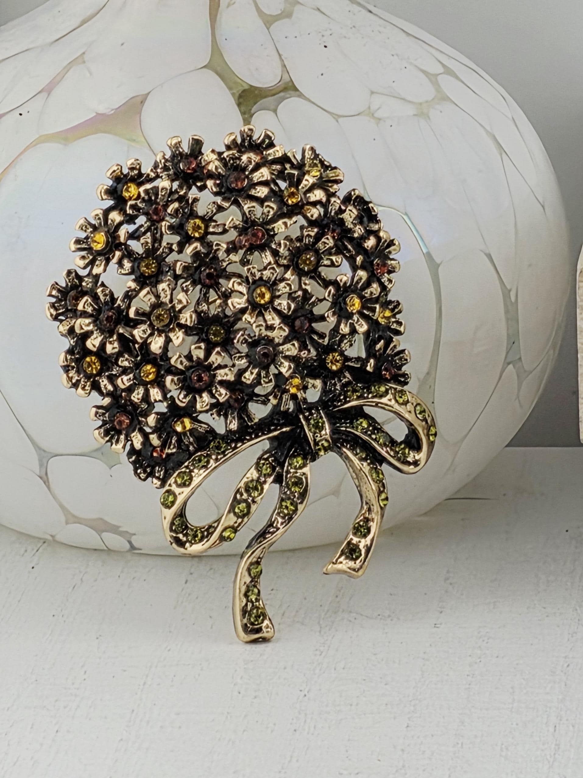 A decorative brooch with a floral design and a green ribbon, placed on a white surface.