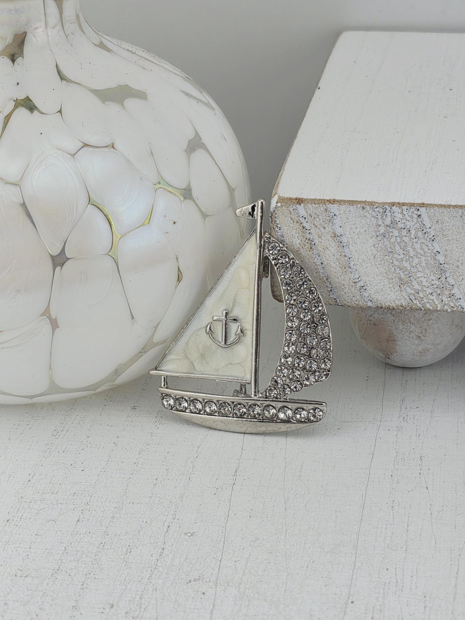 a close-up view of a decorative piece with a silver and white design, including a small anchor-like element and a sparkling crystal accent.