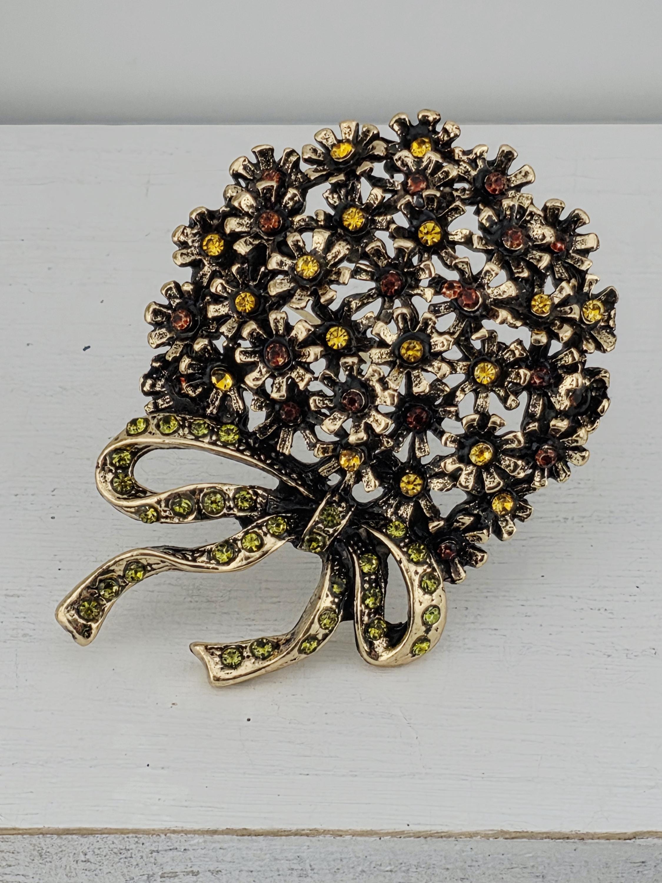 A decorative brooch with a floral design and a ribbon, featuring a variety of colorful gemstones.