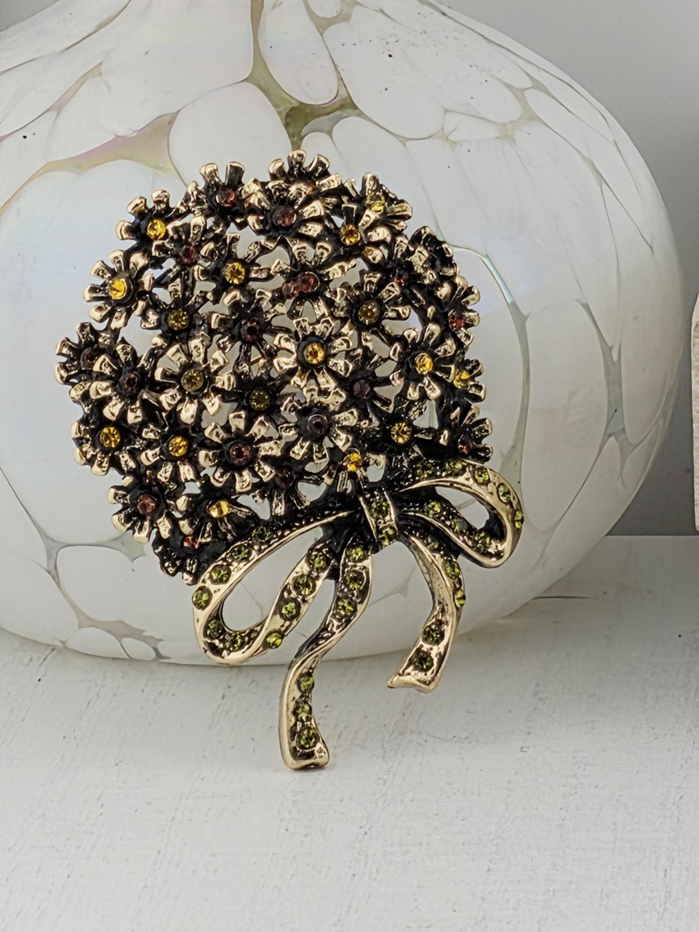 A decorative brooch with a floral design and a green ribbon-like element is displayed against a white background.