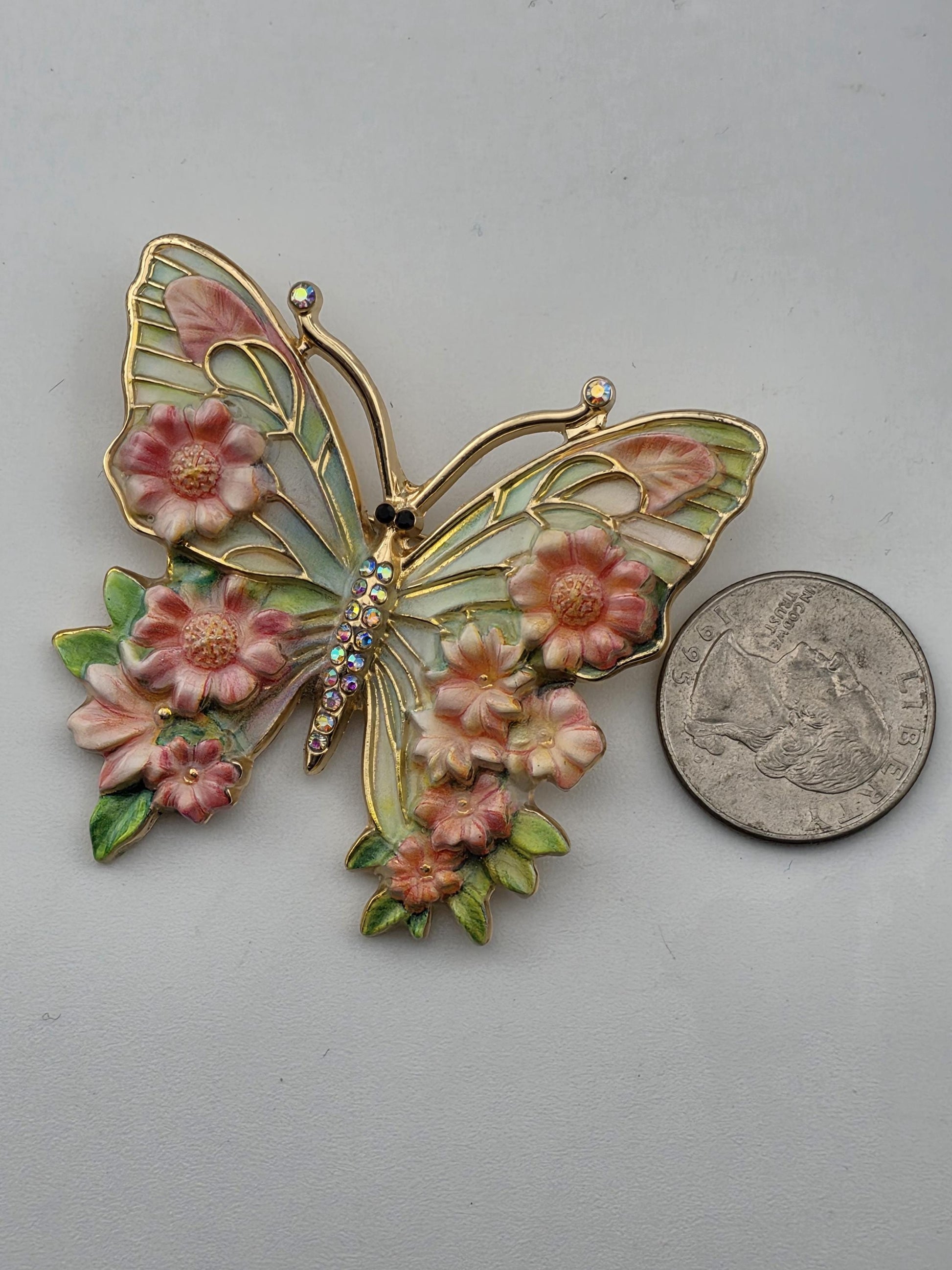 A decorative butterfly brooch with pink flowers and leaves, placed next to a coin.