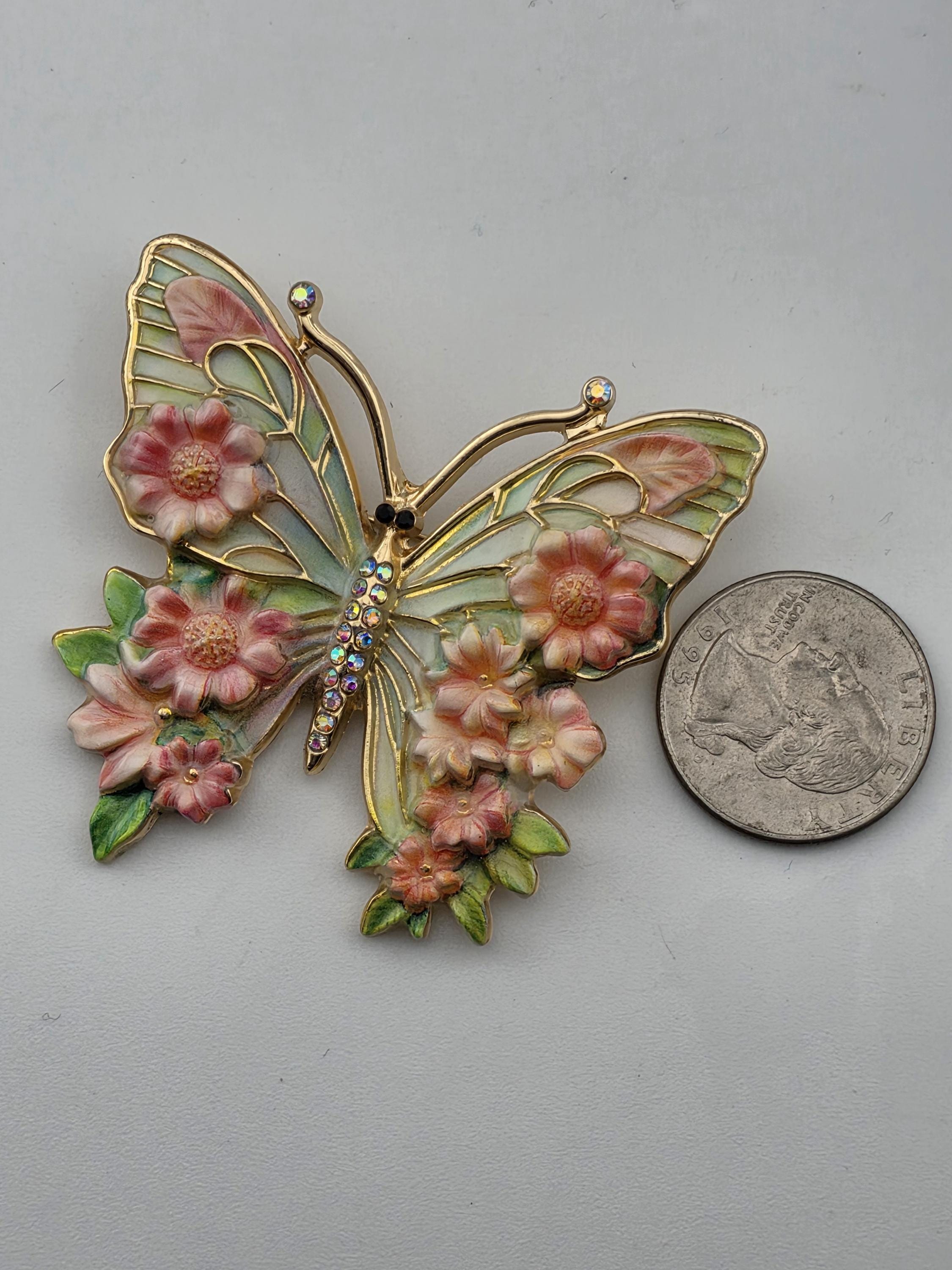A decorative butterfly brooch with pink flowers and leaves, placed next to a coin.