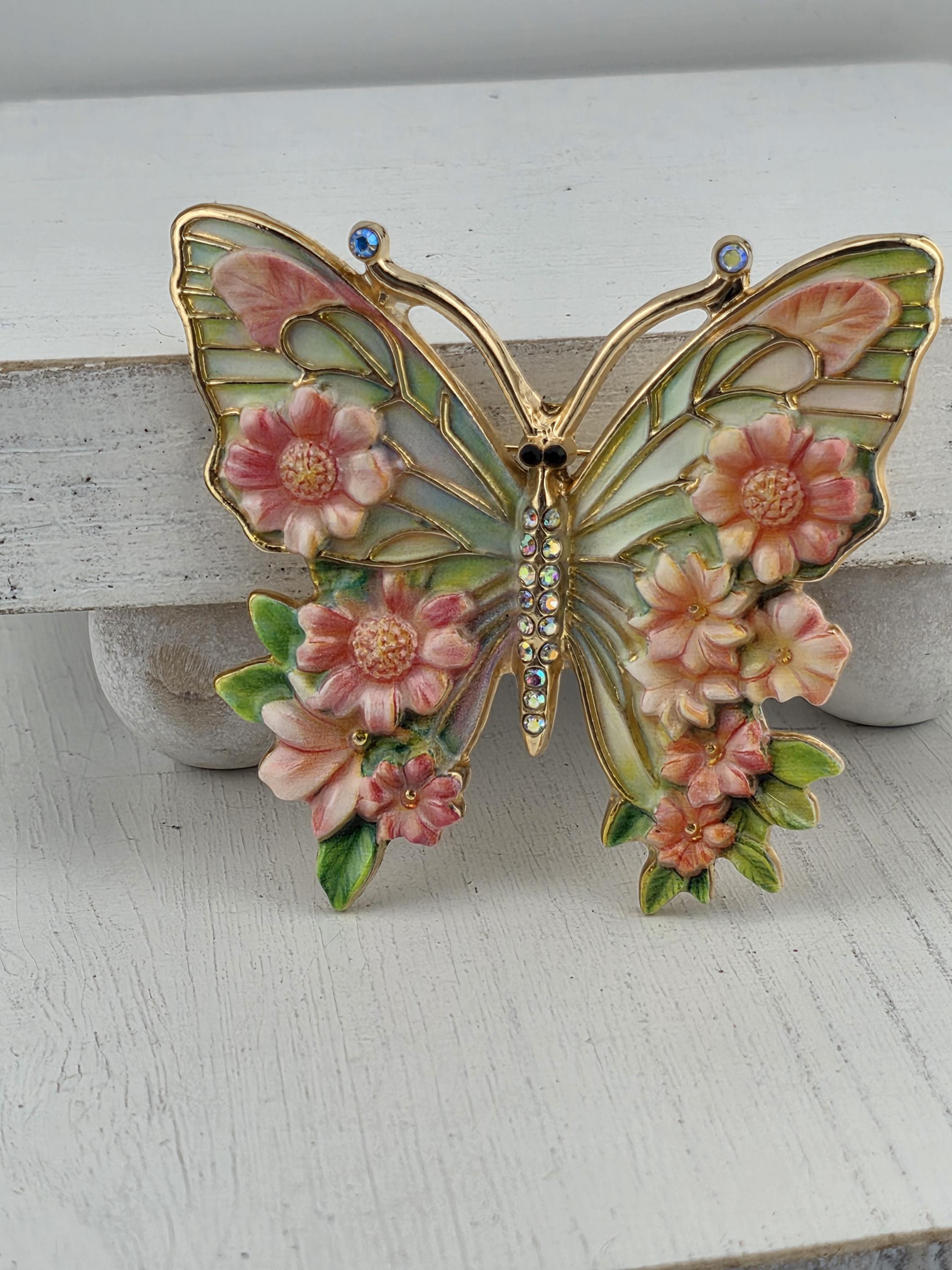 A decorative butterfly brooch with a floral design, featuring pink and green flowers and leaves.