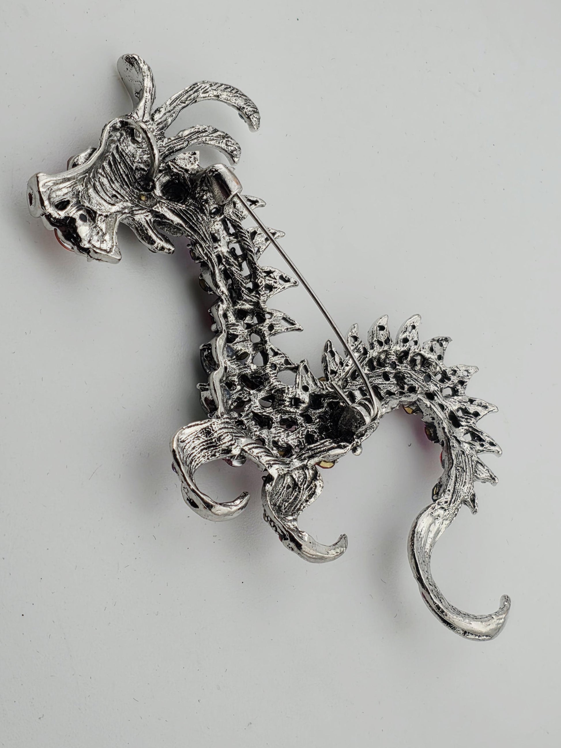 A silver brooch in the shape of a dragon, with intricate details and a crescent moon-like design.