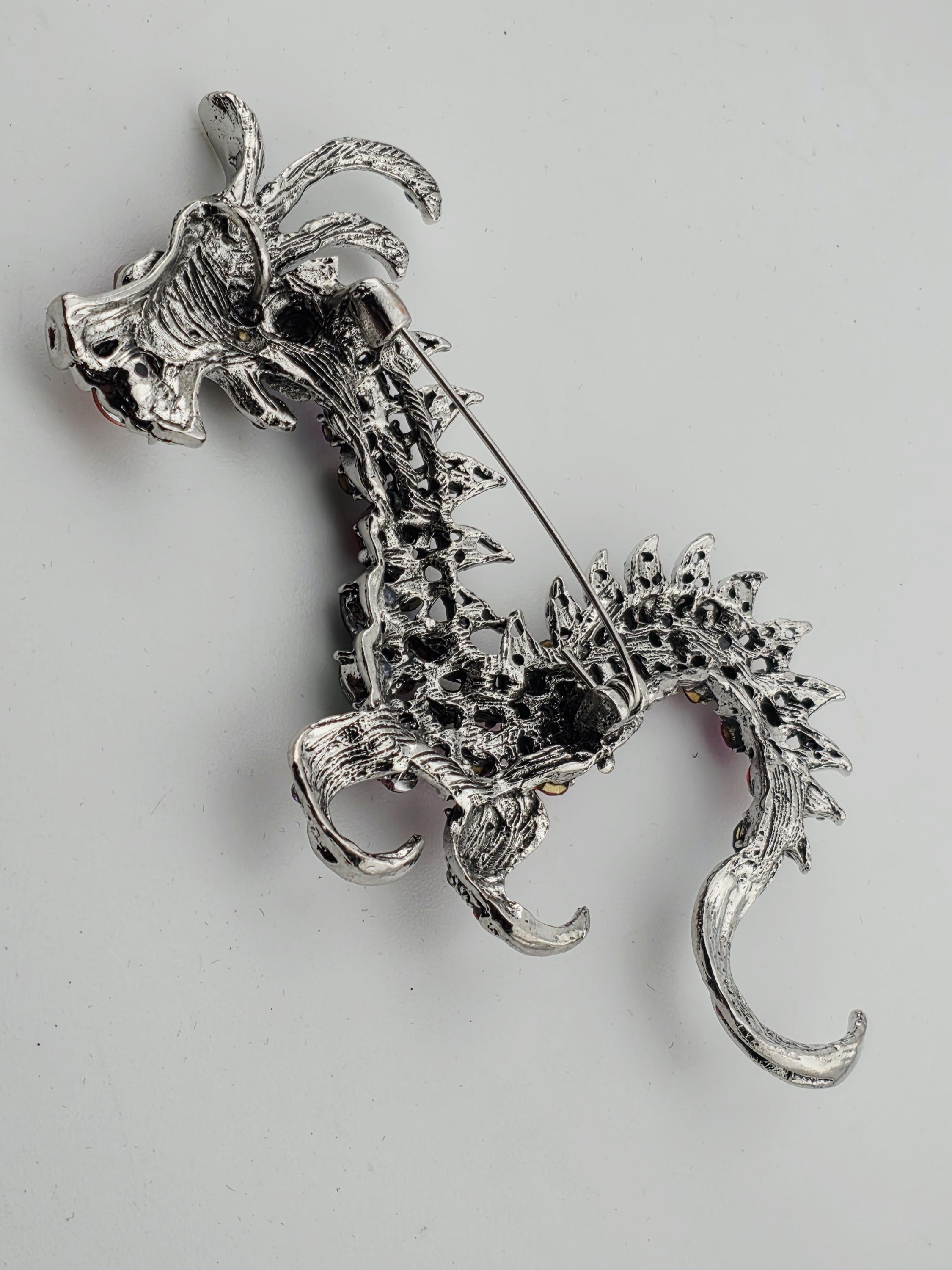A silver brooch in the shape of a dragon, with intricate details and a crescent moon-like design.