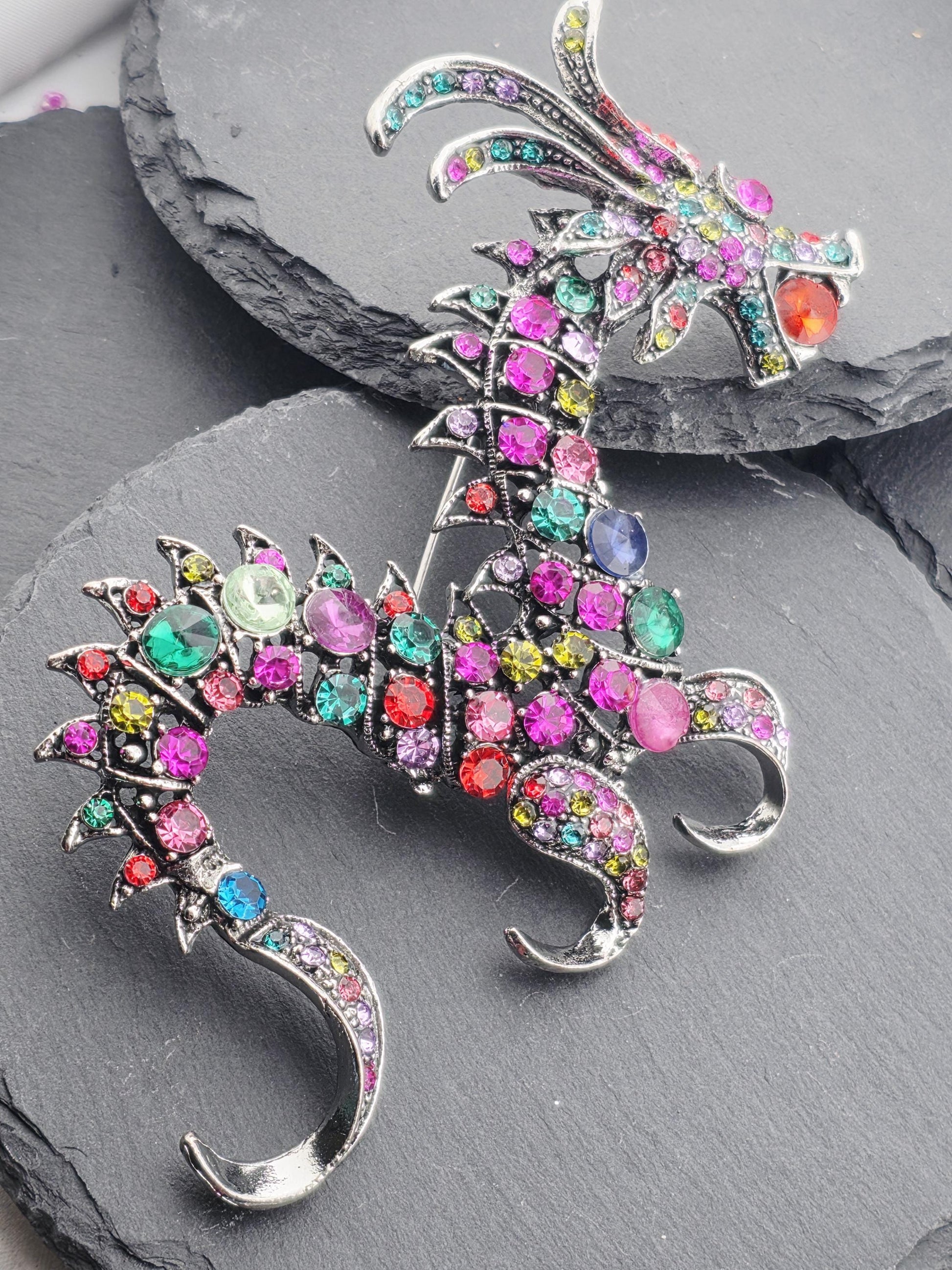 A colorful, ornate brooch with a dragon design, featuring a variety of gemstones and metallic elements.