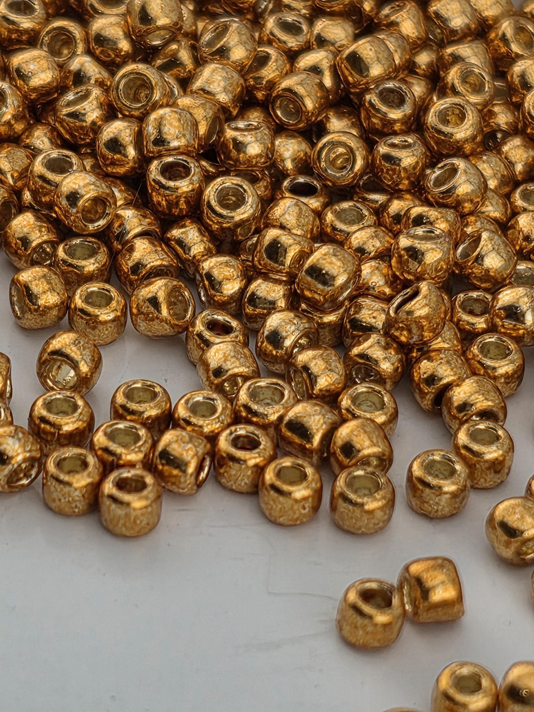 a close-up view of numerous small, shiny gold-colored beads or beads scattered on a white surface.