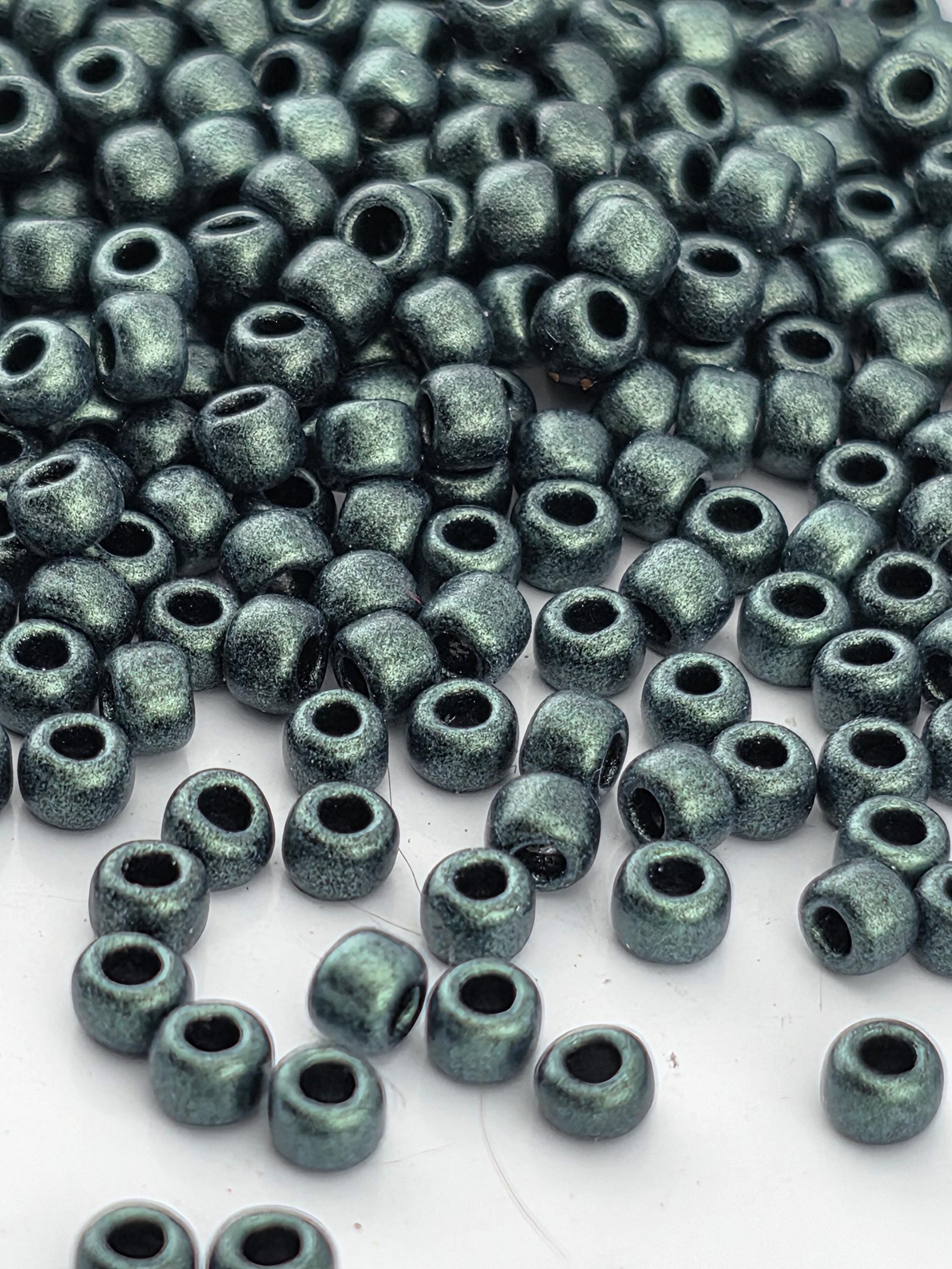 a close-up view of numerous small, shiny beads in various shades of green, scattered across a white surface.