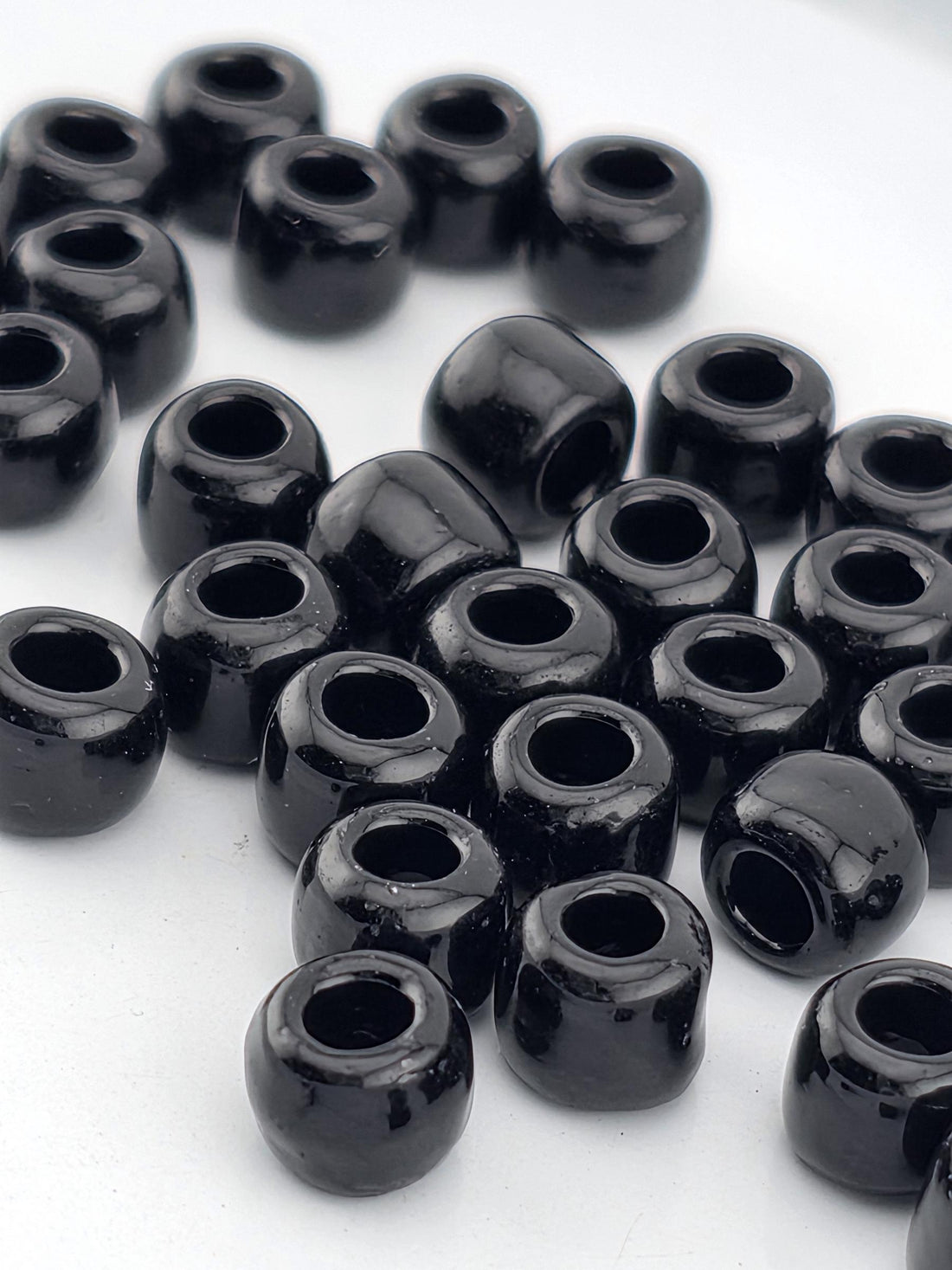 A collection of black beads or objects with a shiny, reflective surface, arranged in a scattered pattern on a white background.