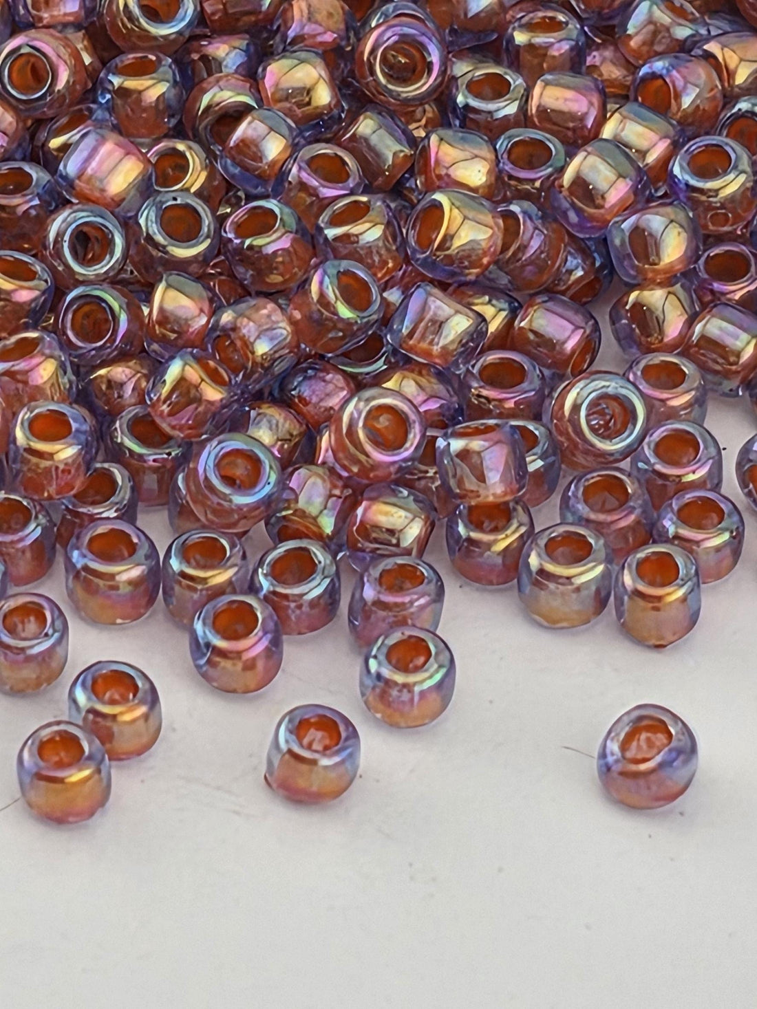 a close-up view of a pile of multicolored glass beads, with a variety of colors including shades of orange, purple, and blue. The beads are scattered across a white surface, creating a visually striking contrast.