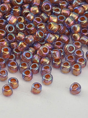 a close-up view of a pile of multicolored glass beads, with a variety of colors including shades of orange, purple, and blue. The beads are scattered across a white surface, creating a visually striking contrast.