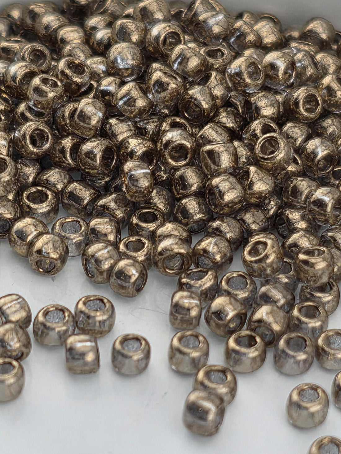 A pile of small, round, metallic beads in various shades of brown, scattered on a white surface.