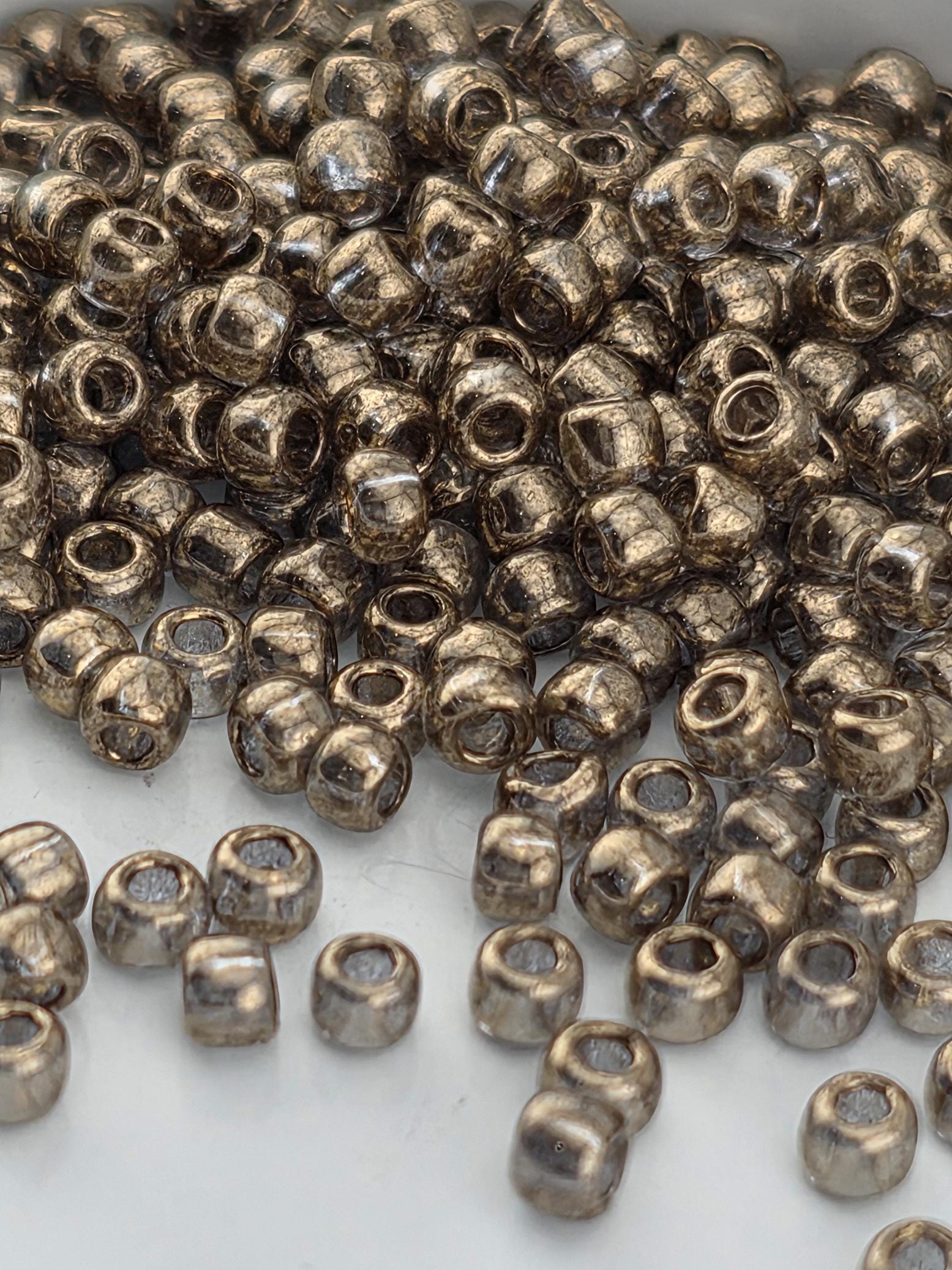 A pile of small, round, metallic beads in various shades of brown, scattered on a white surface.
