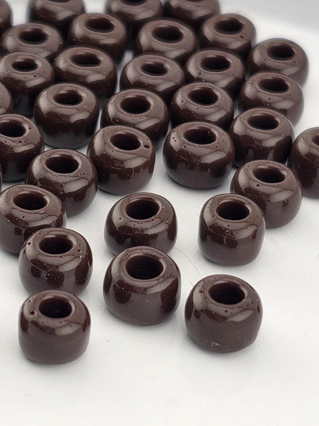 a close-up view of numerous dark brown, glossy beads arranged in a pattern on a white surface.