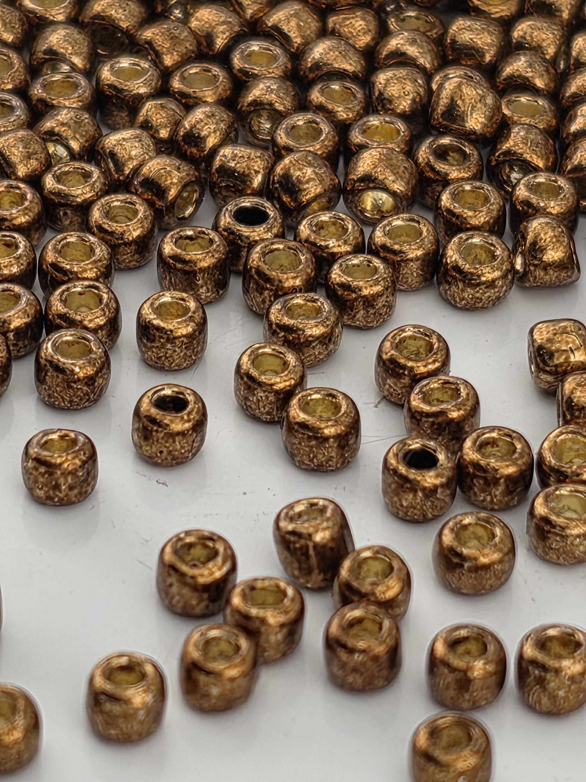 a close-up view of numerous small, round, golden-colored beads or beads scattered across a white surface.