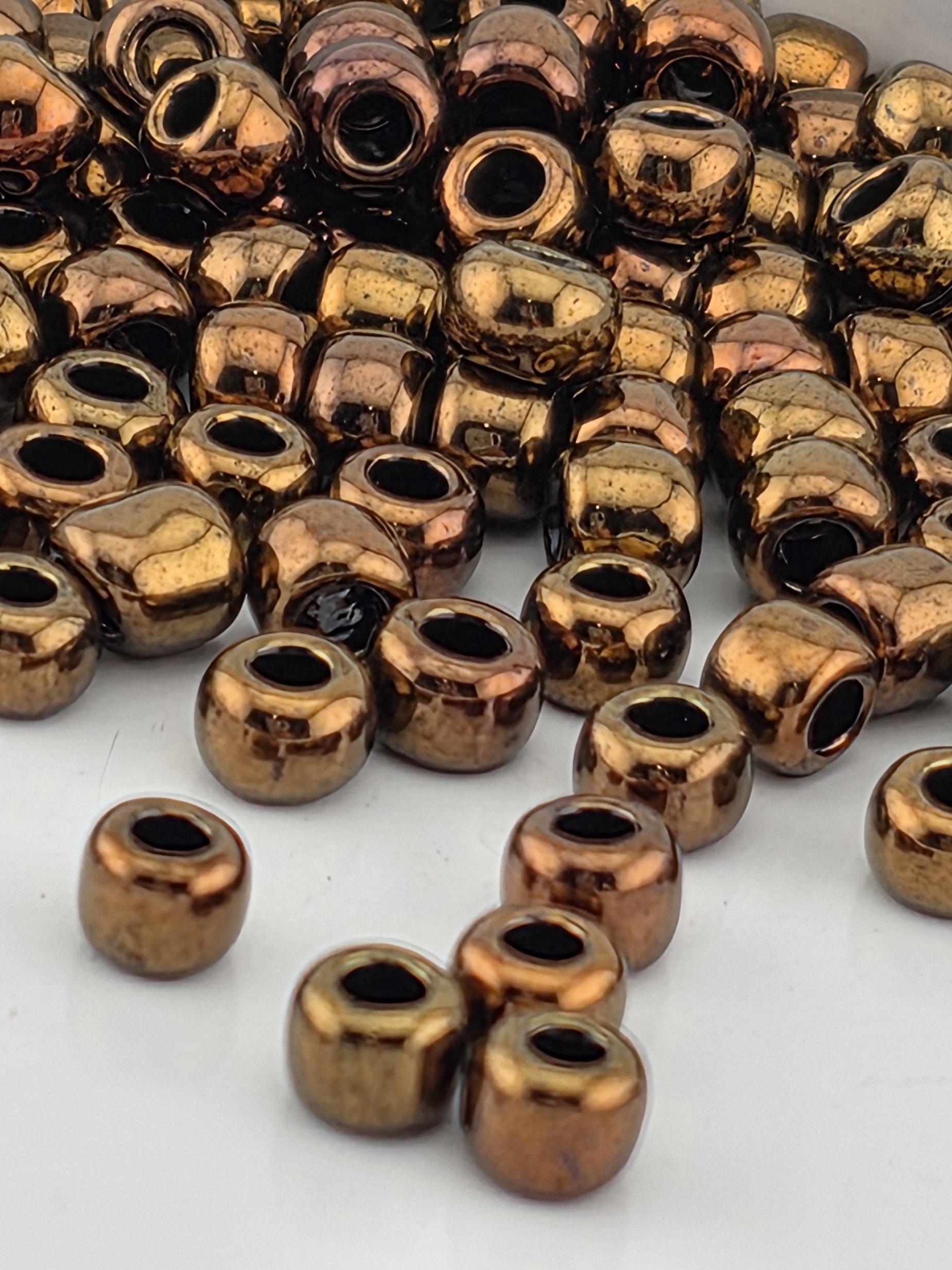 a collection of small, shiny, metallic beads in various shades of brown and copper, scattered on a white surface.
