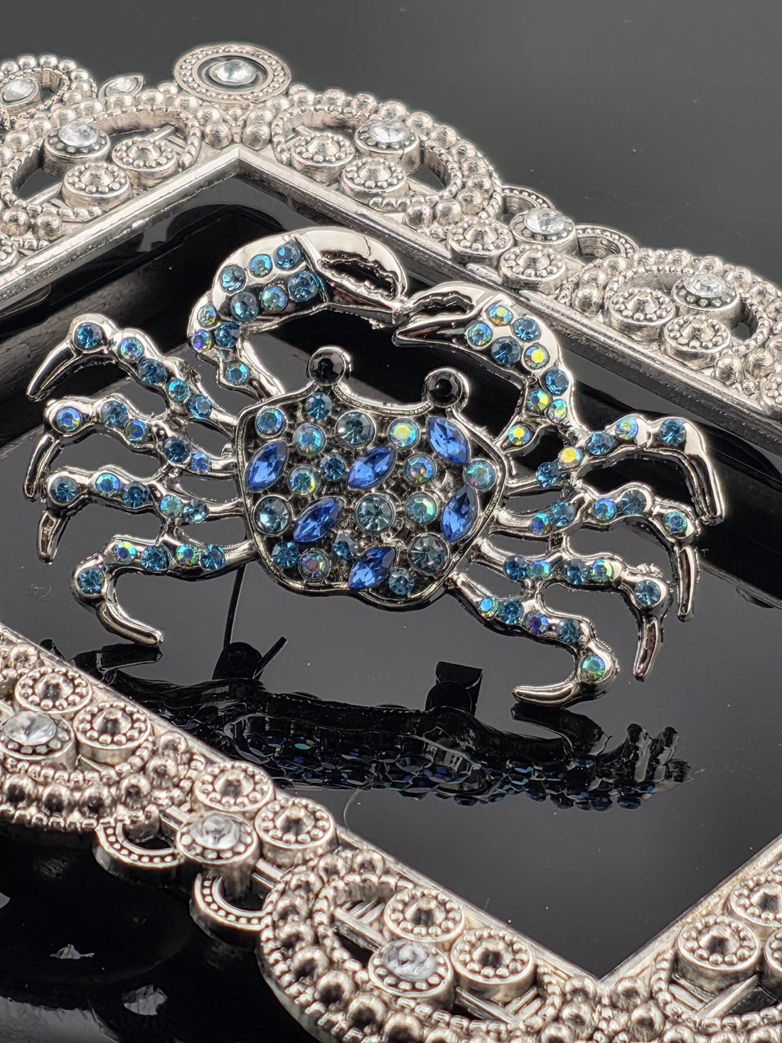 a close-up view of a decorative crab-shaped piece of jewelry, adorned with numerous blue gemstones. The crab is intricately designed and appears to be the focal point of the image.