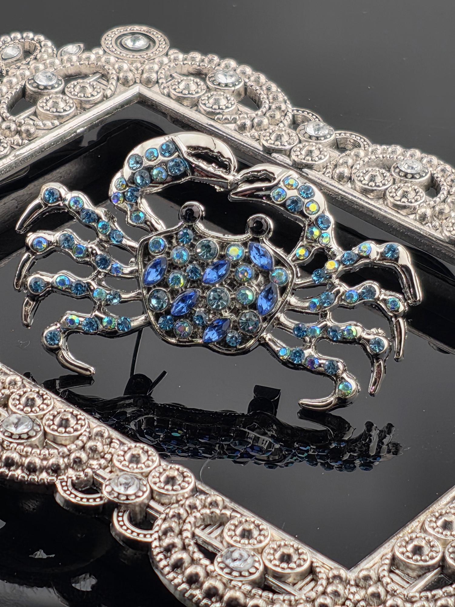 a close-up view of a decorative crab-shaped piece of jewelry, adorned with numerous blue gemstones. The crab is intricately designed and appears to be the focal point of the image.